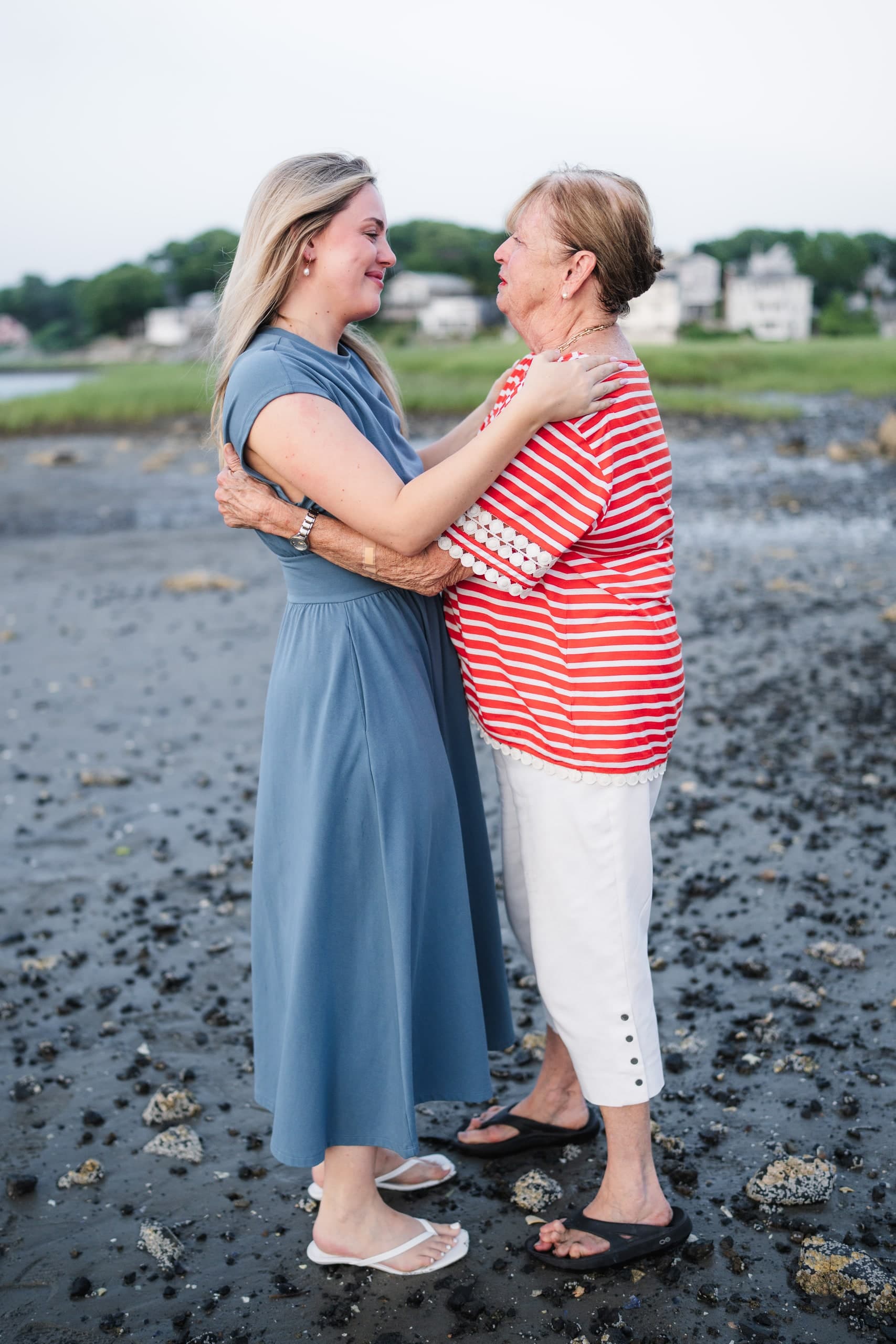 The newly engaged woman embracing an older family member on the beach, face to face.