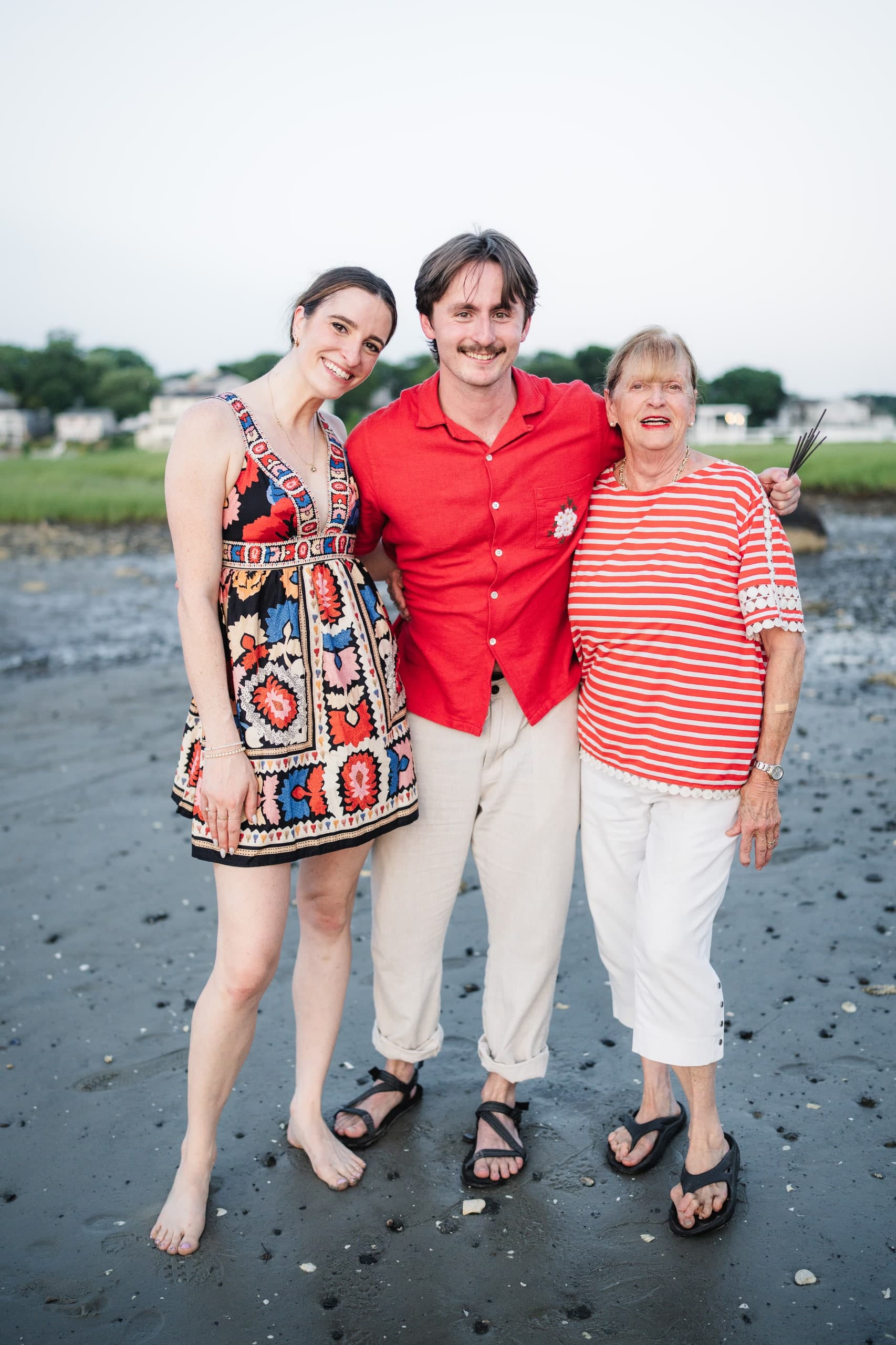 The newly engaged woman, her partner, and an older family member laughing together on the beach.