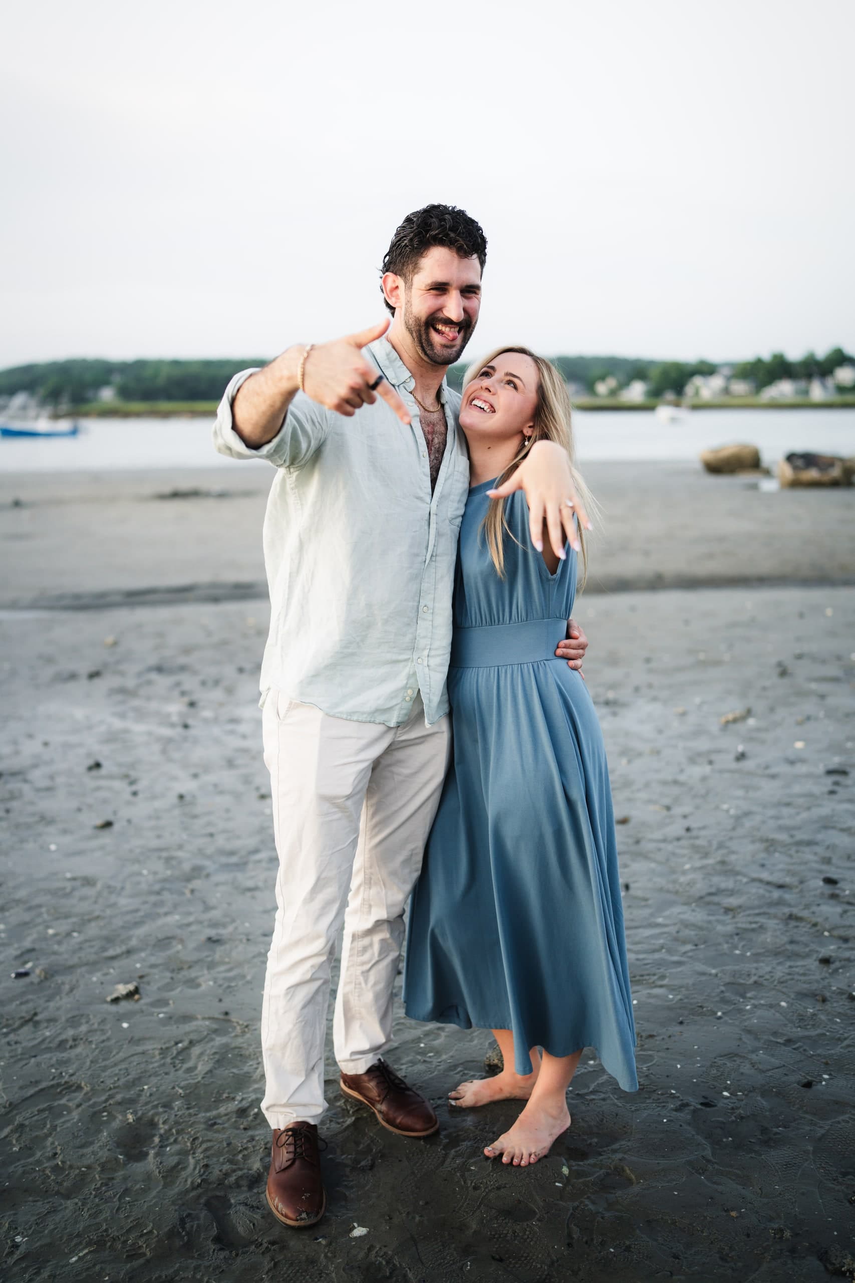 The newly engaged couple laughing playfully, him pointing at the camera, her arm raised.