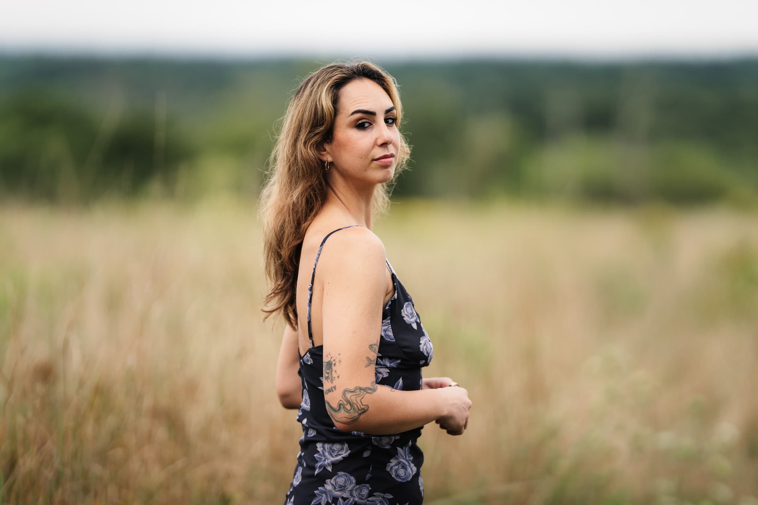 A woman in a floral dress standing in a golden, backlit field at sunset.