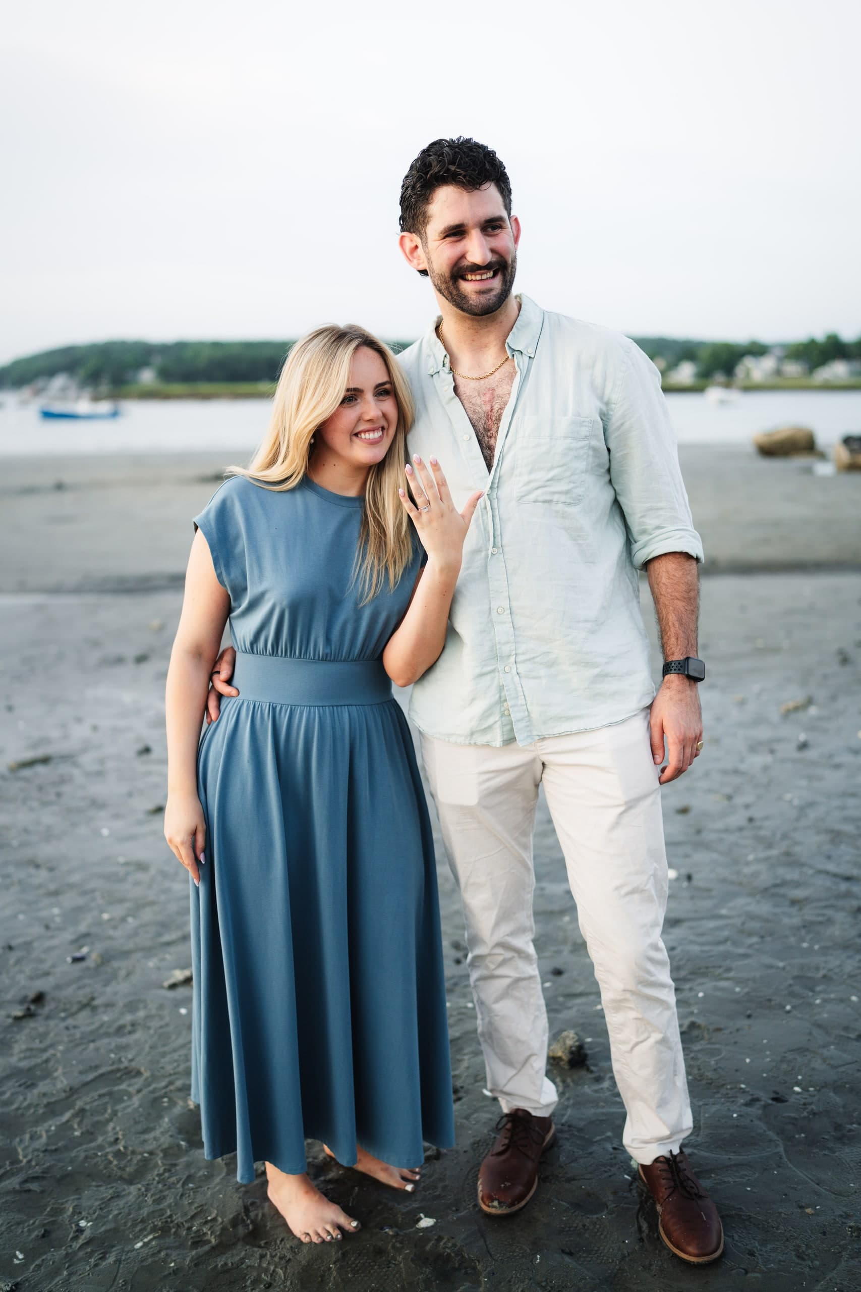 The newly engaged couple laughing together on the beach, a second frame of the same moment.