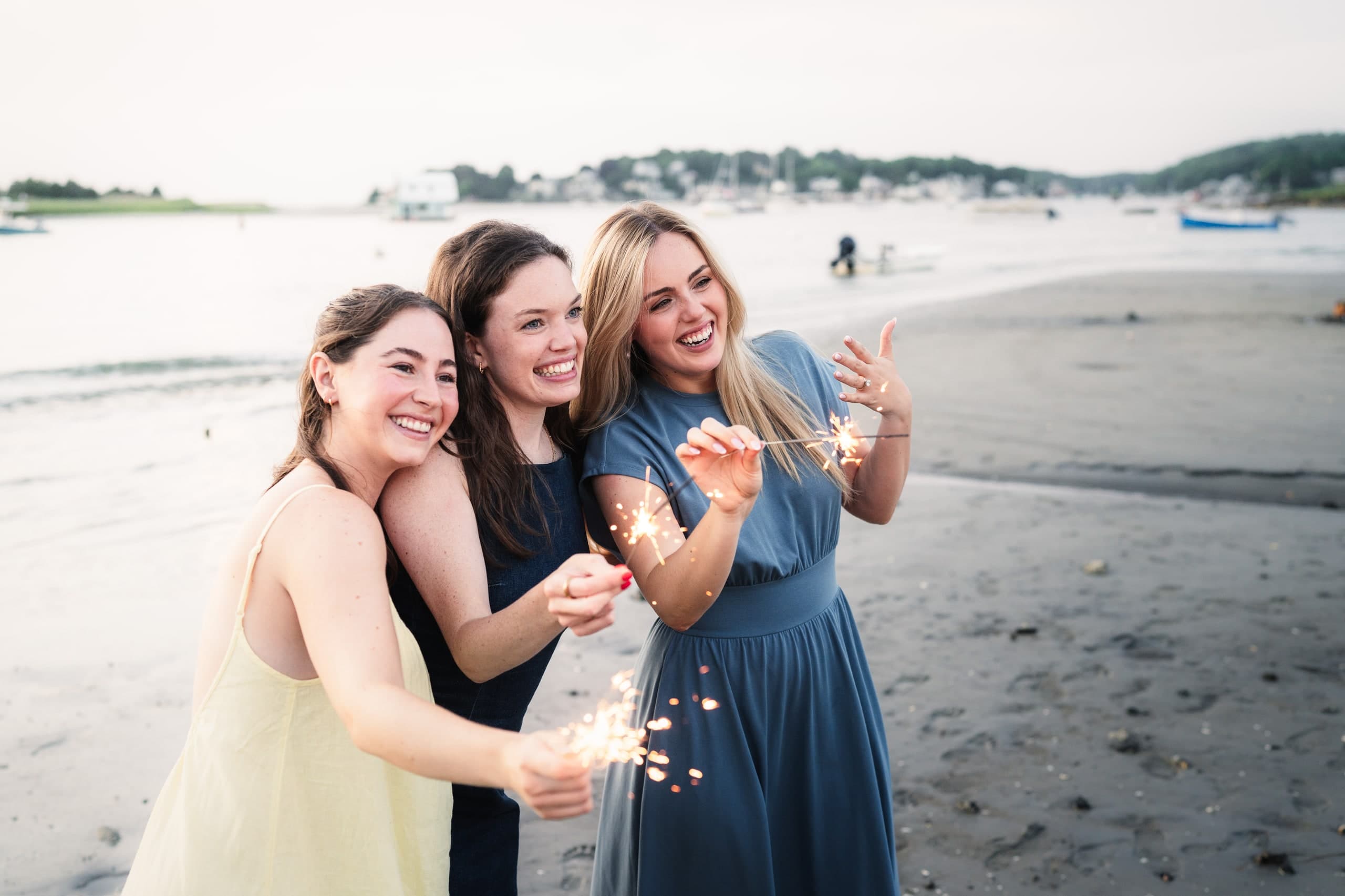 Friends celebrating with sparklers on a dark beach after a proposal.