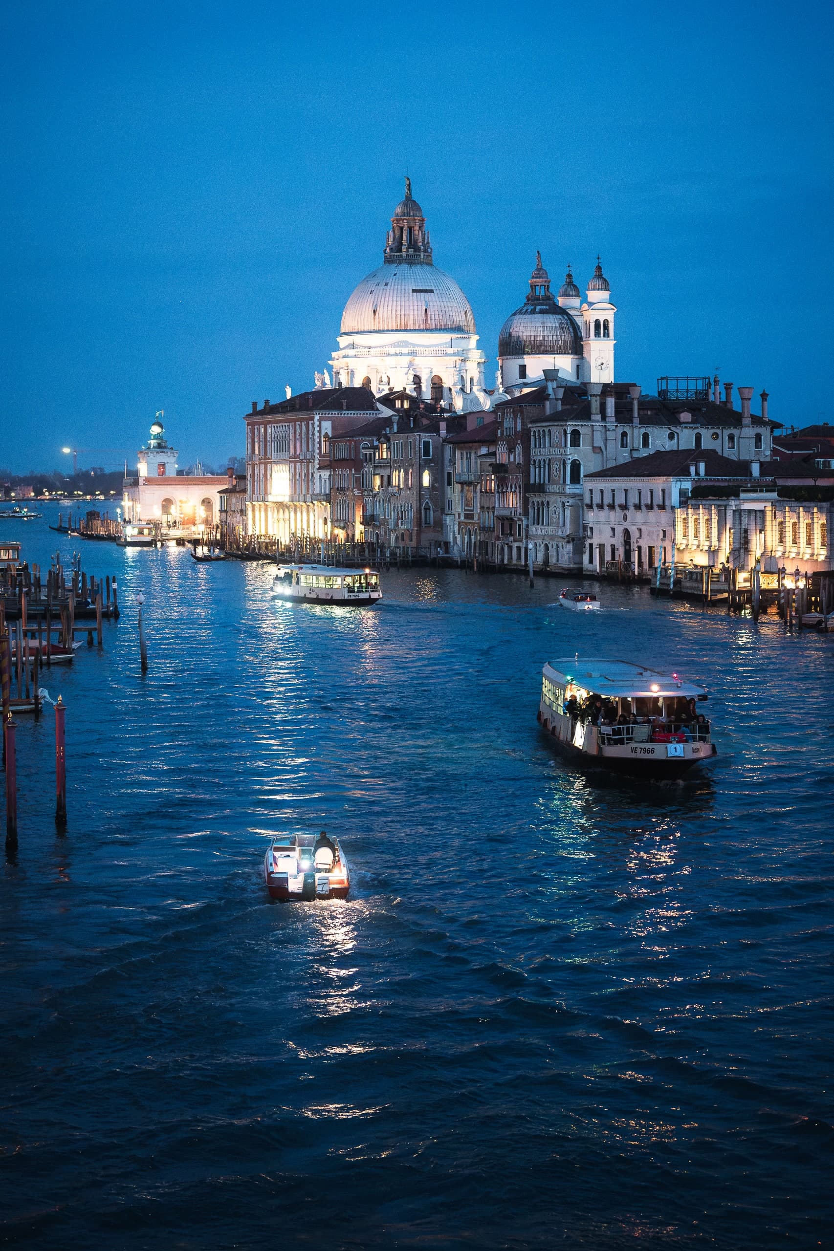 Two boats on a Venice canal at blue hour, the Santa Maria della Salute dome lit in the distance.