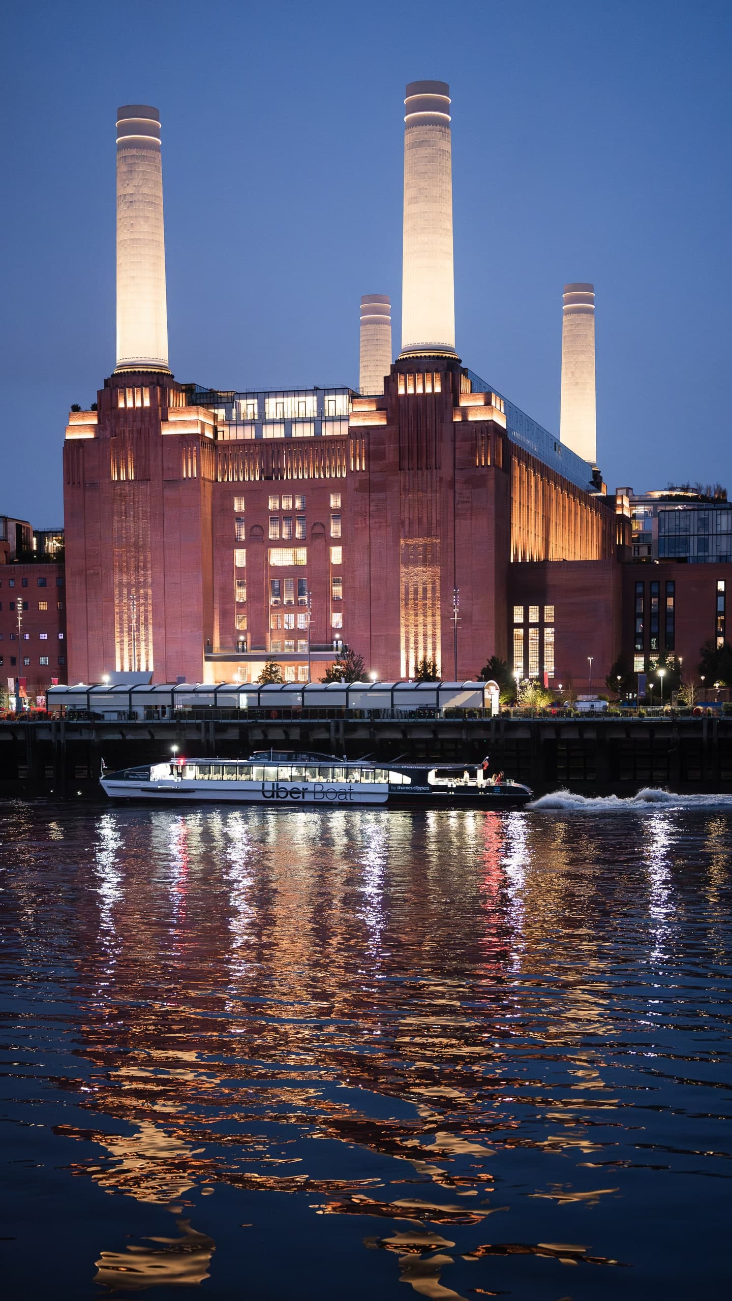 Battersea Power Station lit at night, reflected in the Thames.