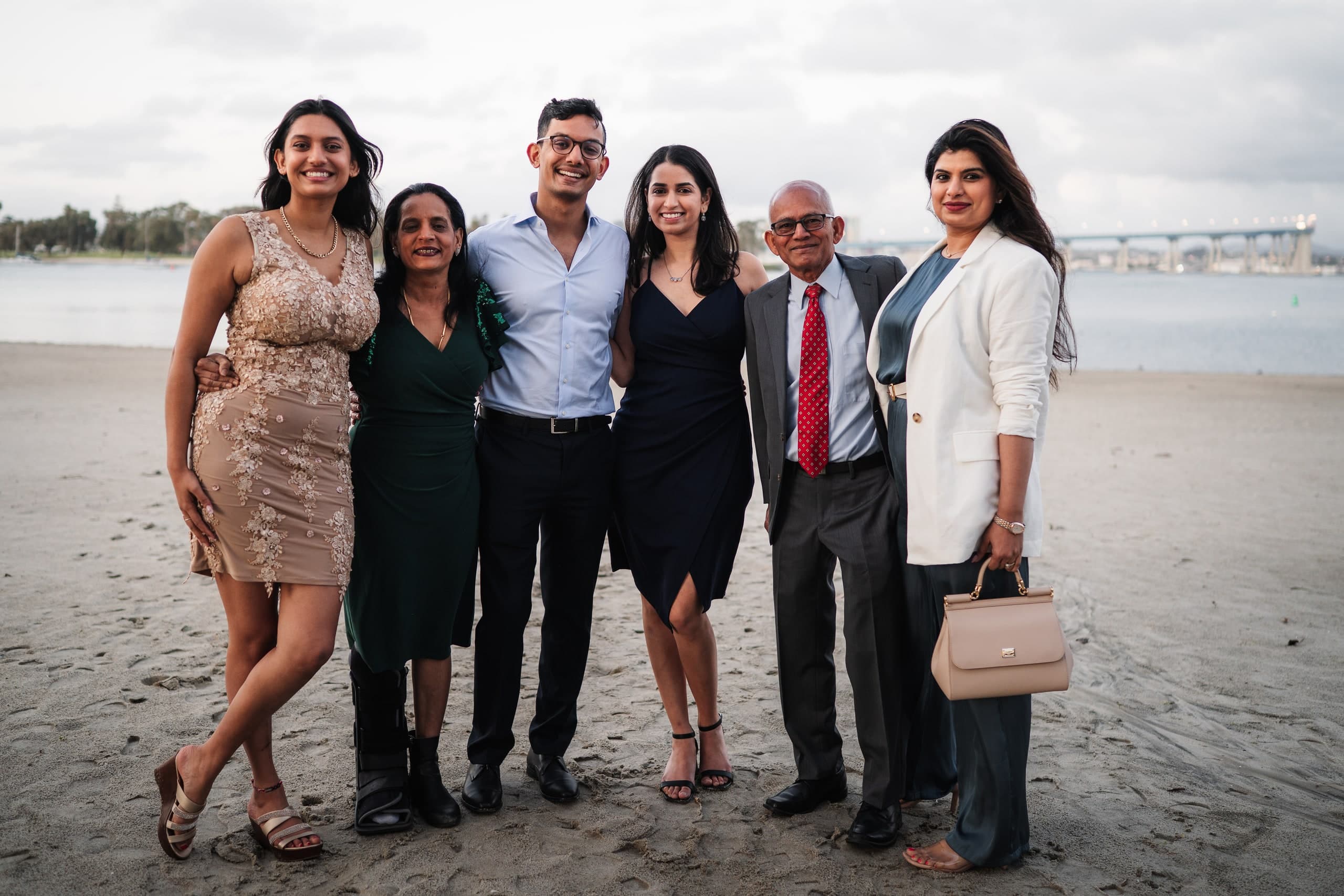 Six friends dressed up and posing together on the beach at dusk.