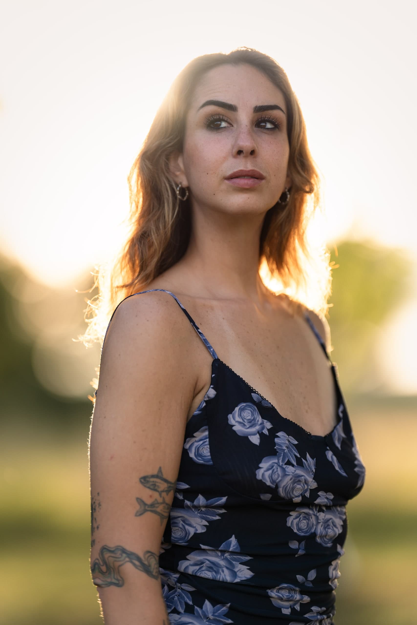 A close portrait of a woman in a blue floral dress, a tattoo visible on her forearm.