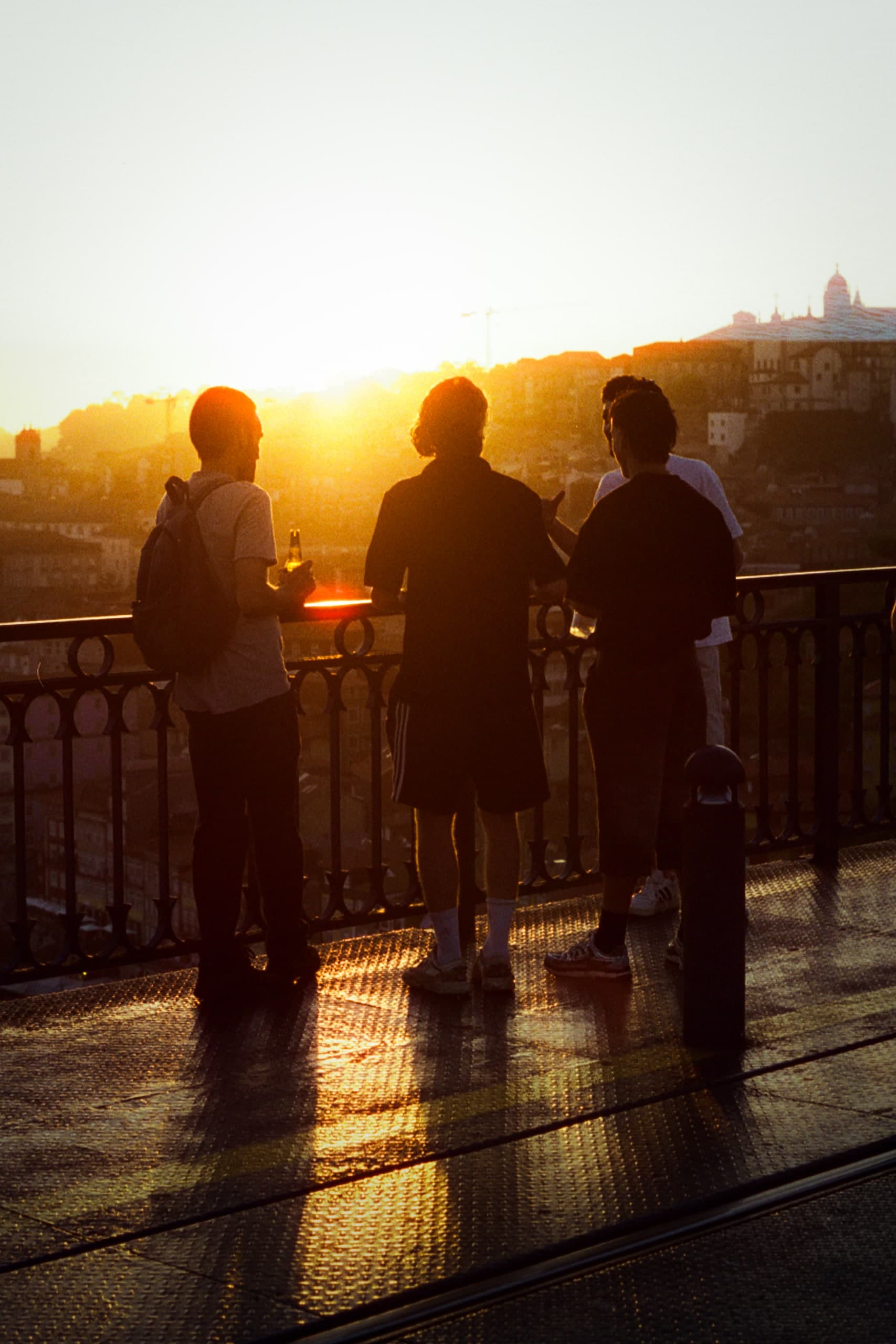 Three friends leaning on a bridge railing, silhouetted against the setting sun.
