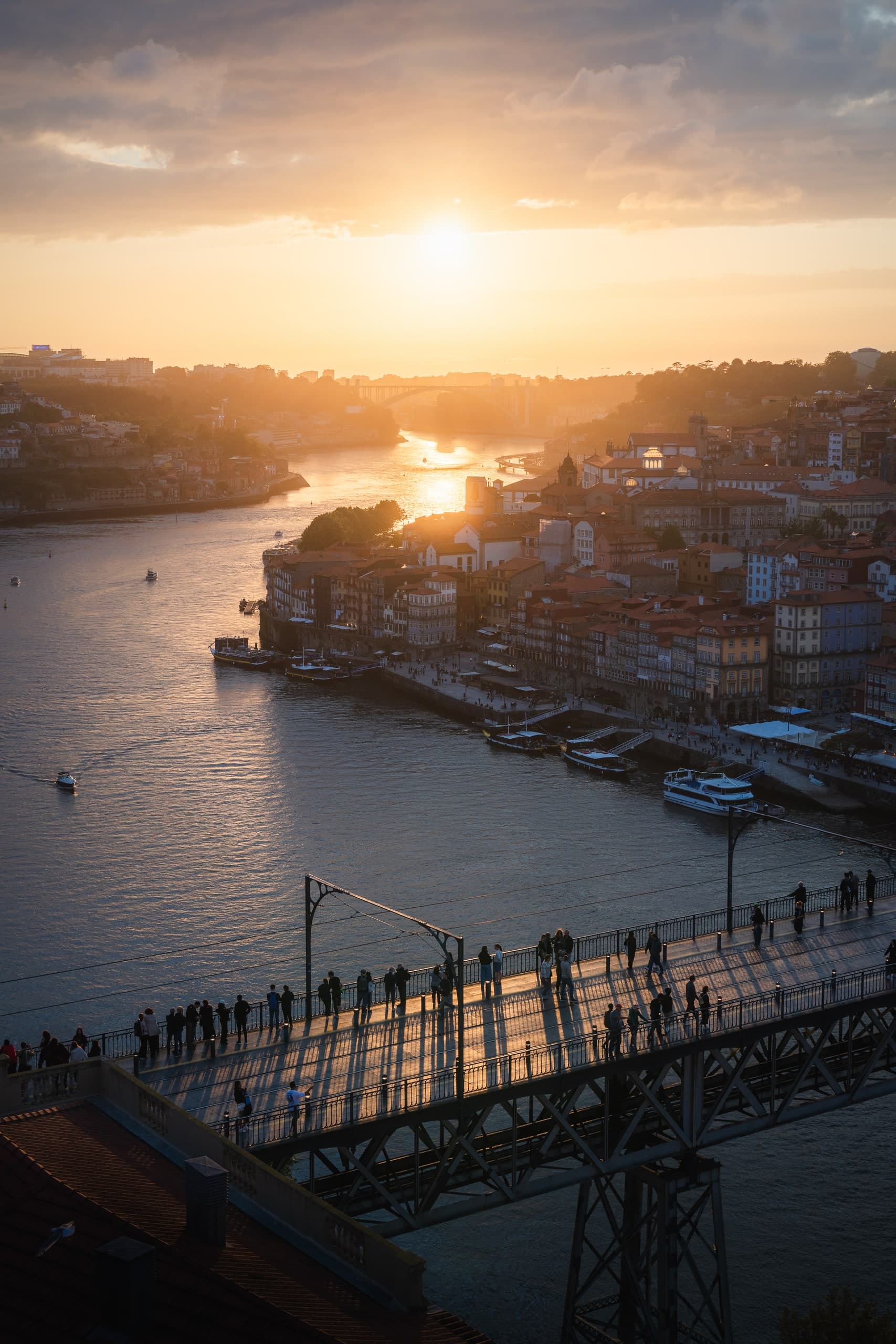 The sun setting over the Douro River in Porto, a pedestrian bridge crossing in silhouette.