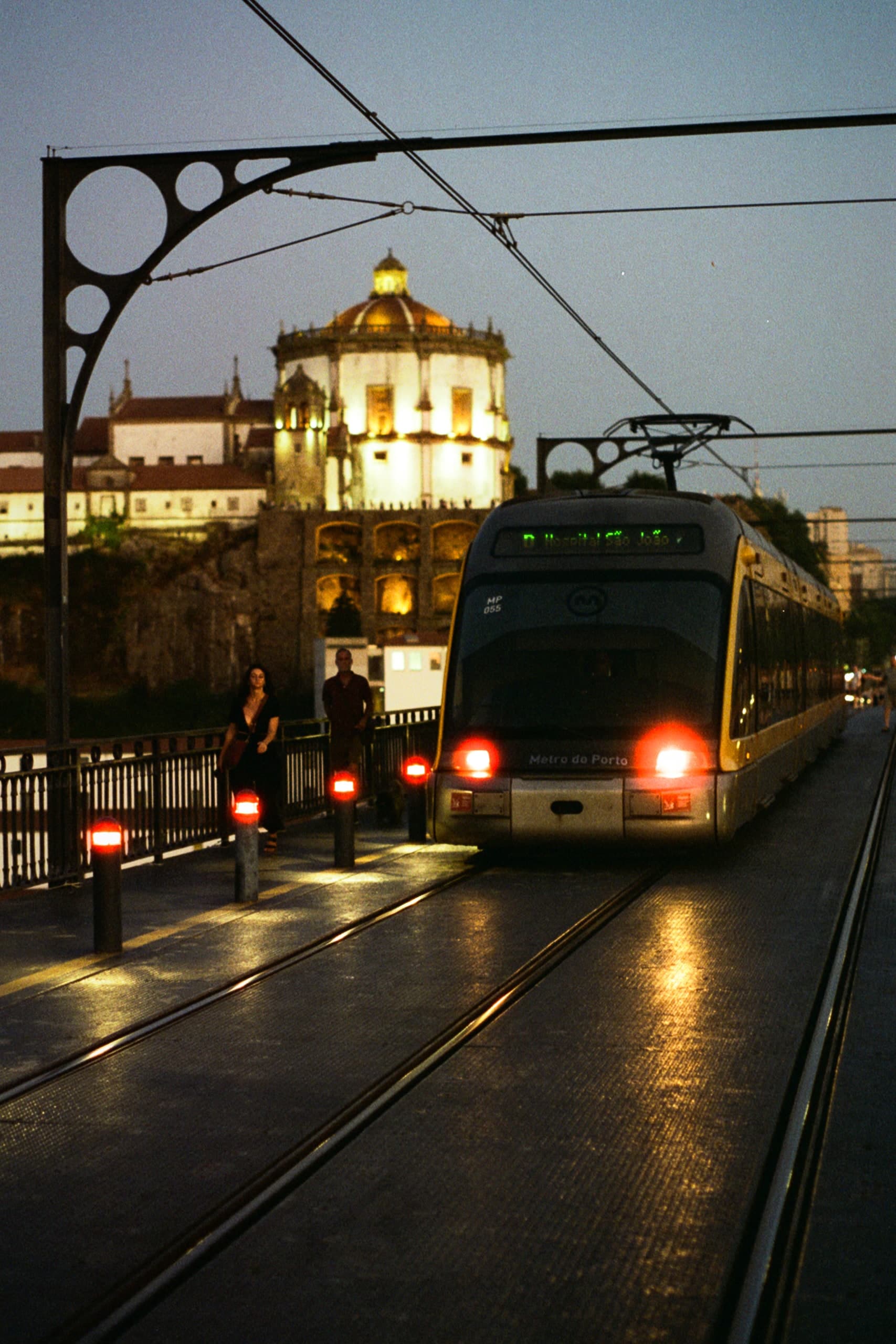 A tram arriving at a station in Porto, a domed church lit behind it.