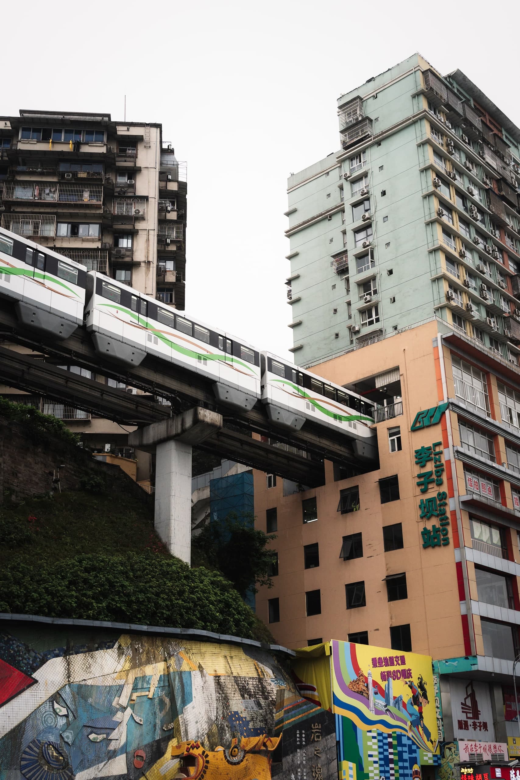 A monorail passing beside apartment buildings on a hillside street in China.