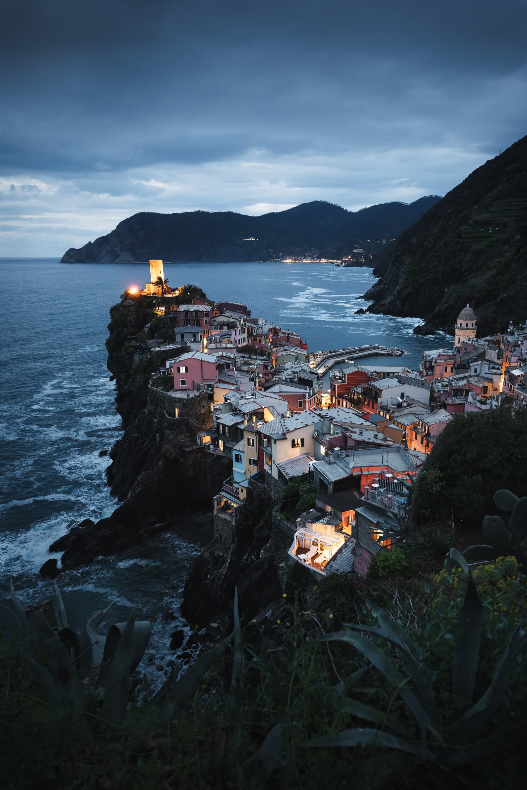 The cliffside town of Vernazza, Cinque Terre, lit at dusk above the sea.