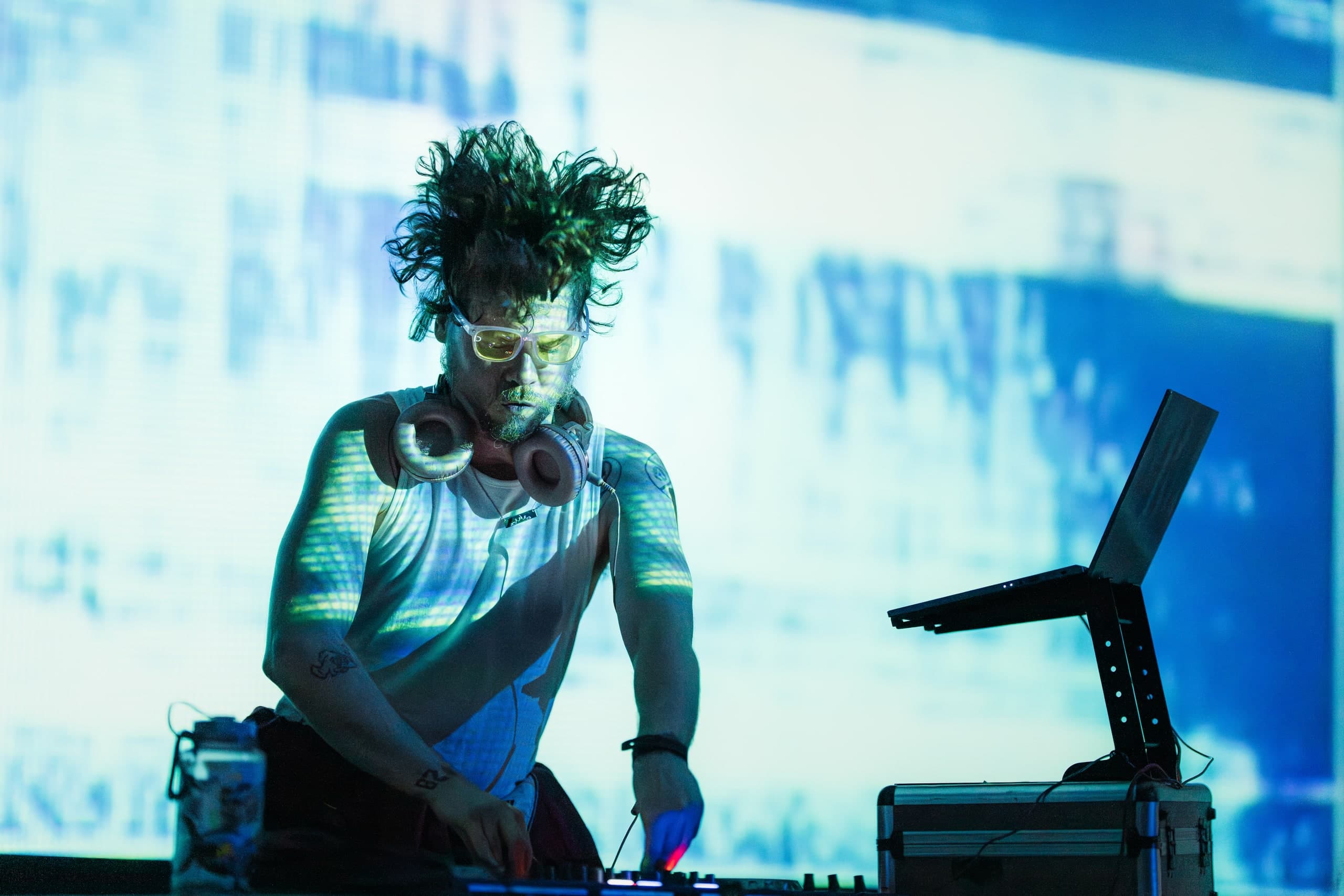 A DJ lit in green and blue, performing in front of a video wall.