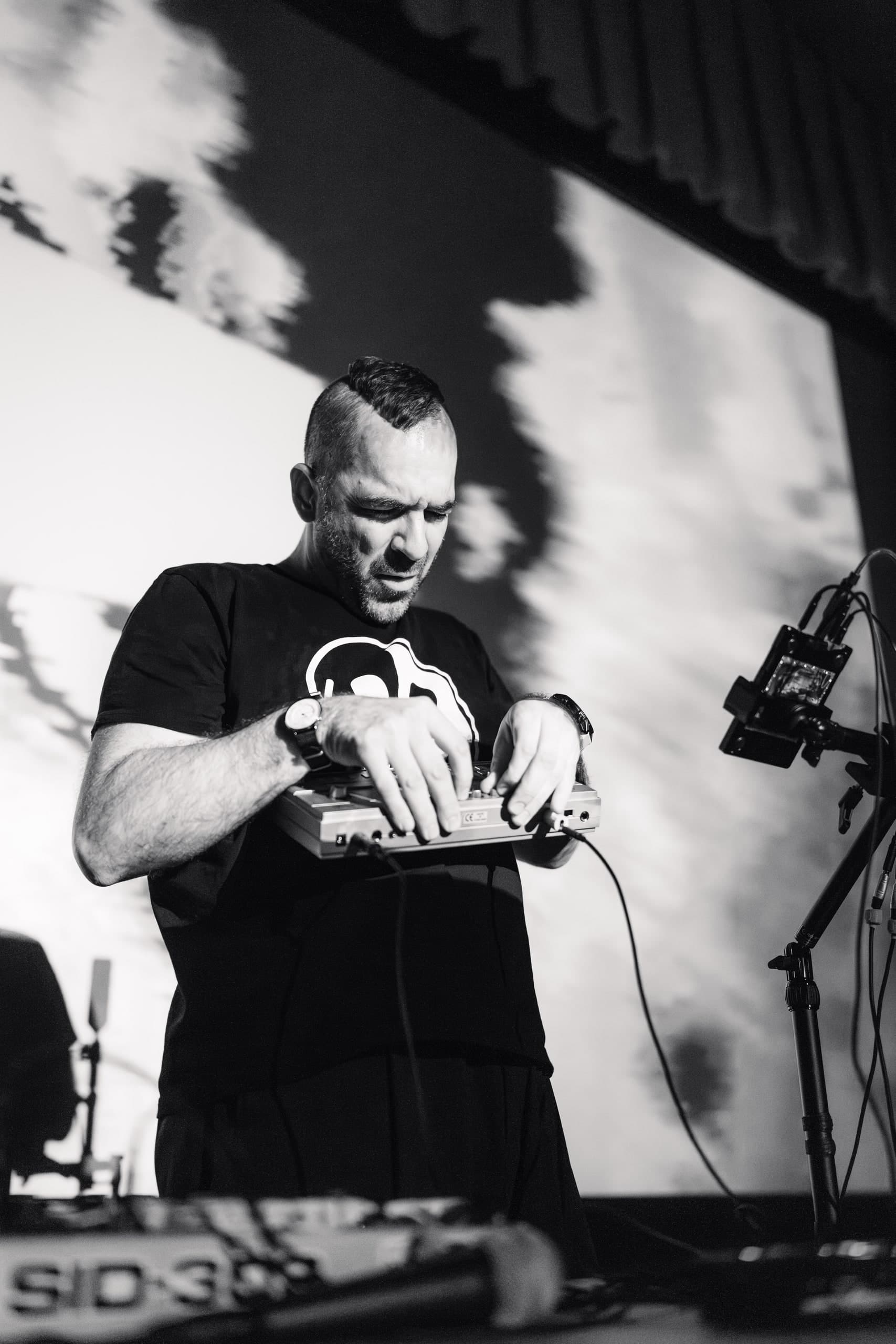 A black-and-white photo of a DJ working a mixing console at a concert.