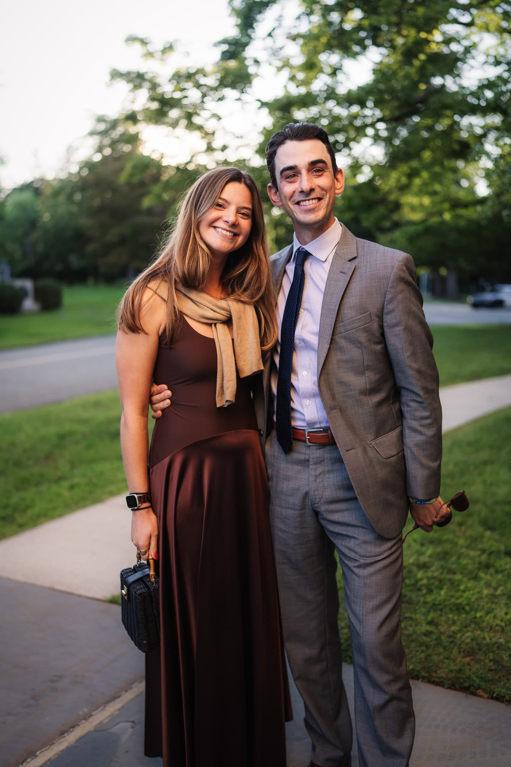 A couple standing close together outdoors at dusk, smiling.