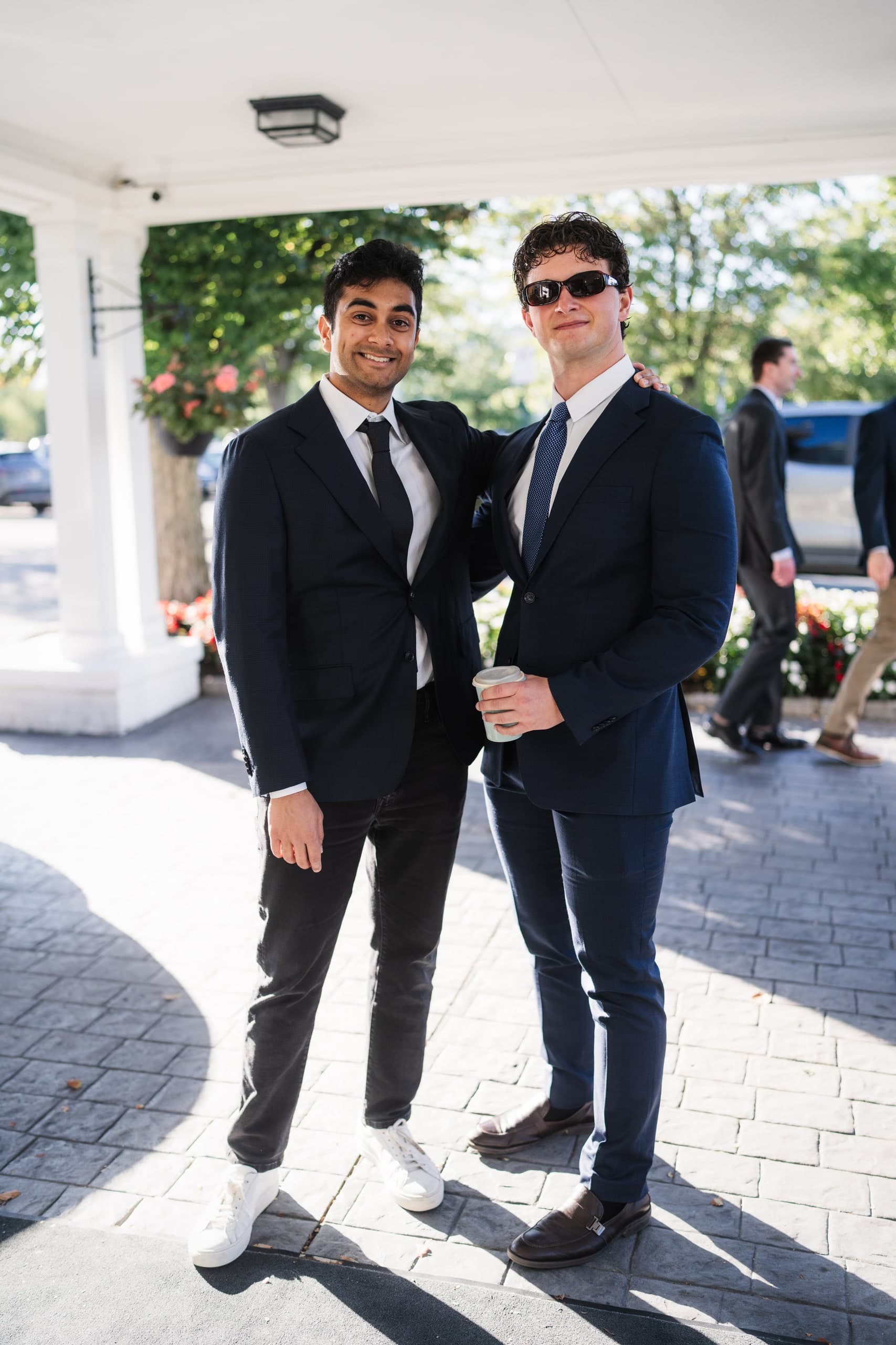 Two friends embracing outside, both in dark suits, laughing.