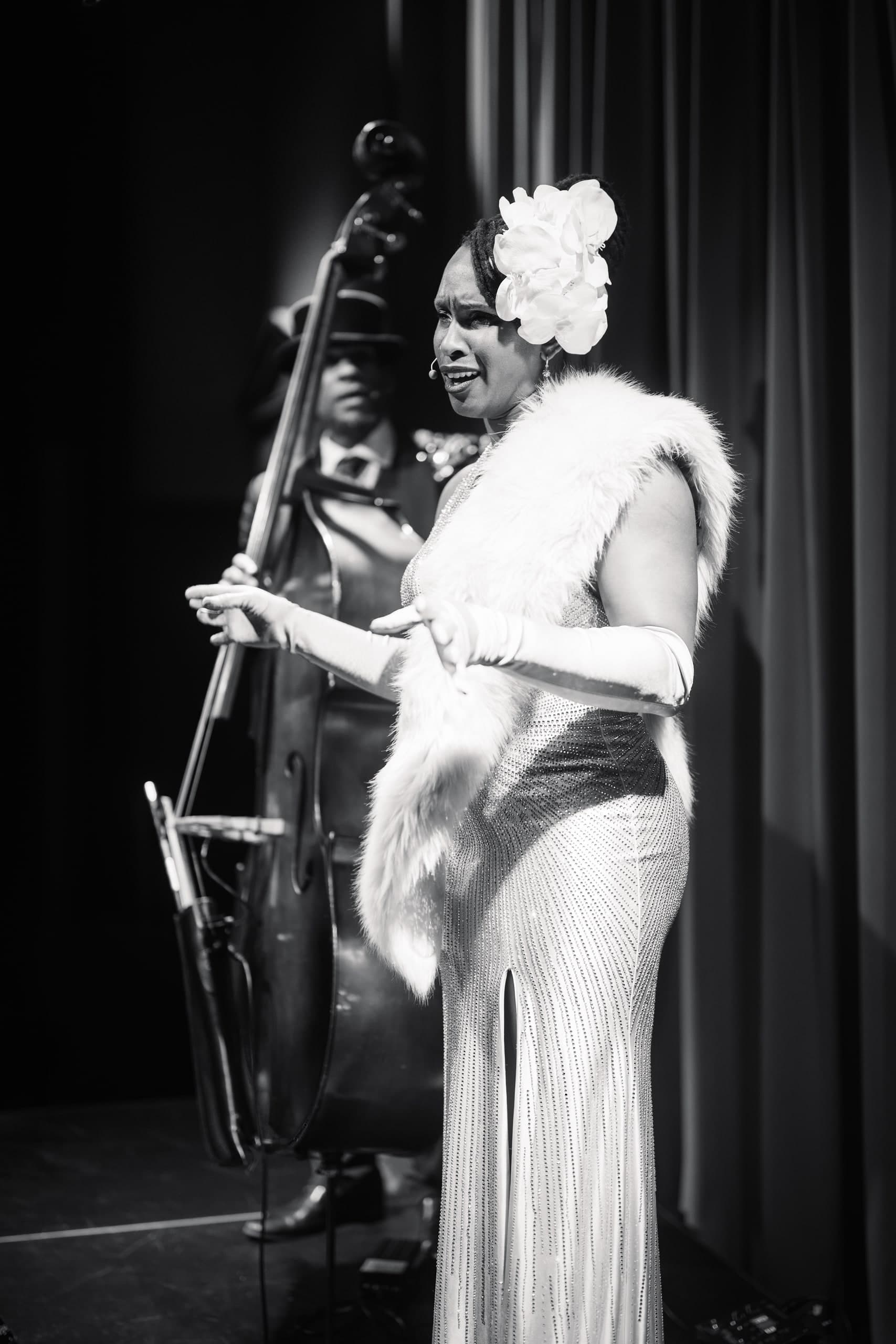 A black-and-white photo of a performer in a feathered costume playing an upright bass.