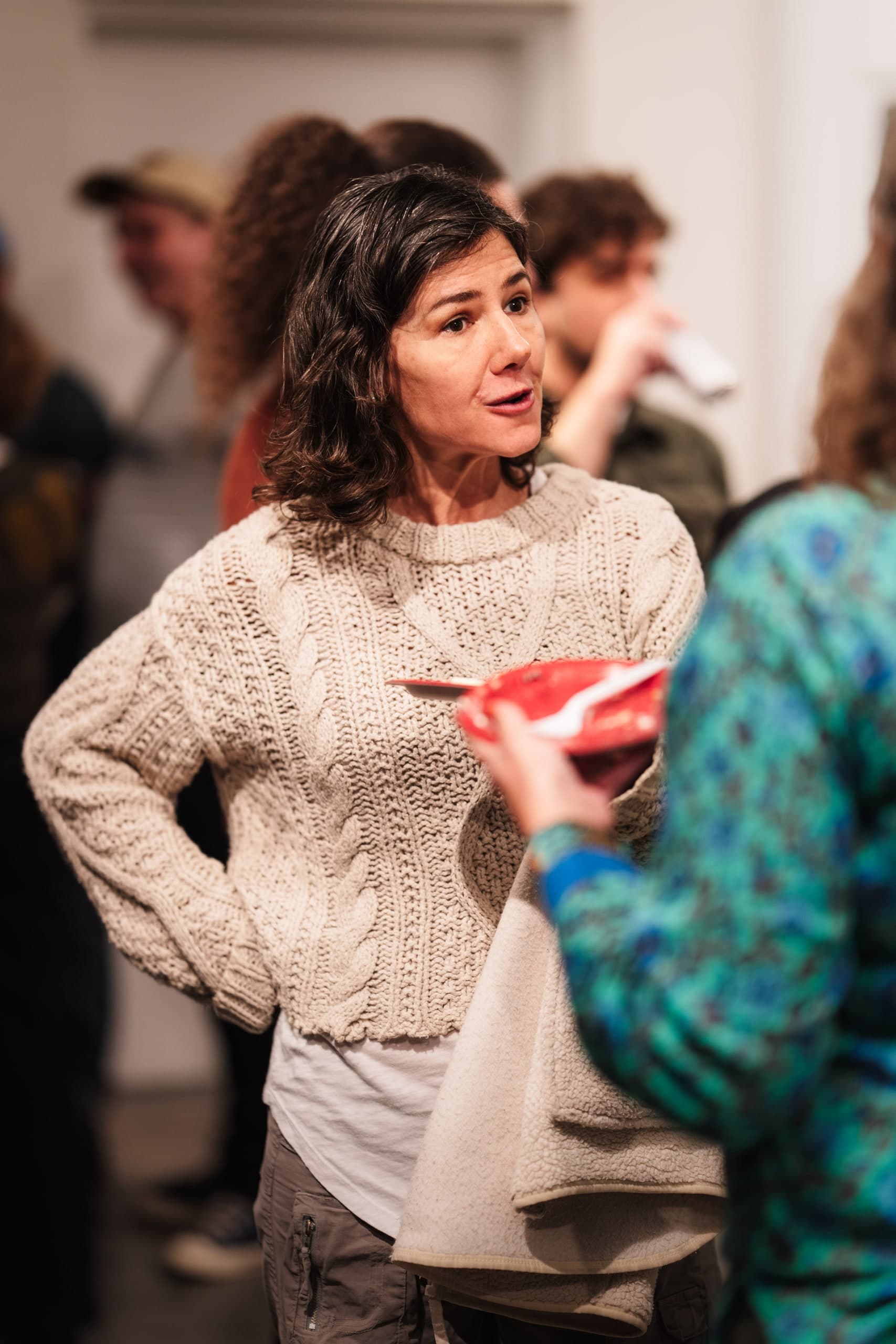 Two women in coats talking at an indoor reception.