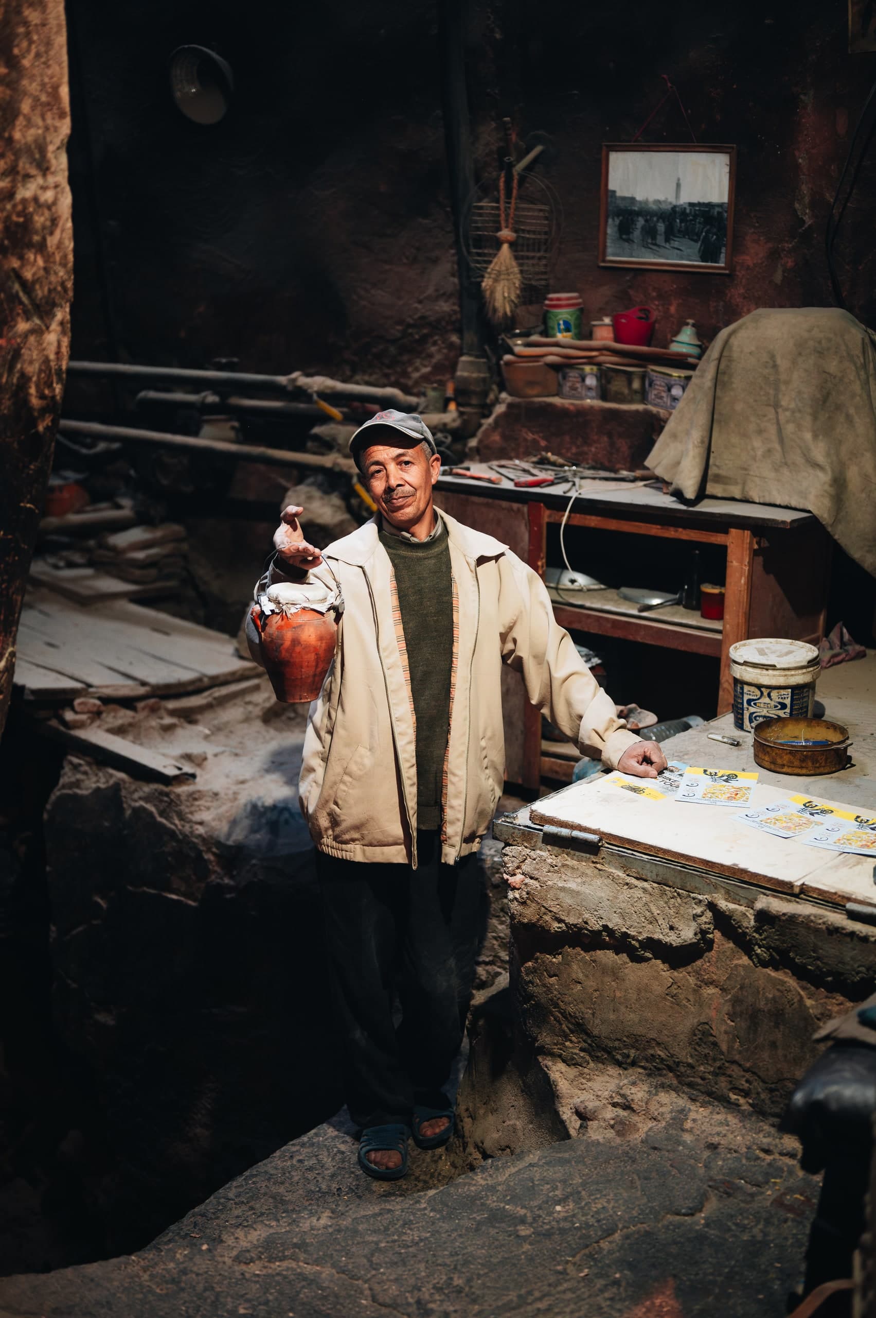 A man standing in his workshop doorway, arranging pottery on the bench beside him.