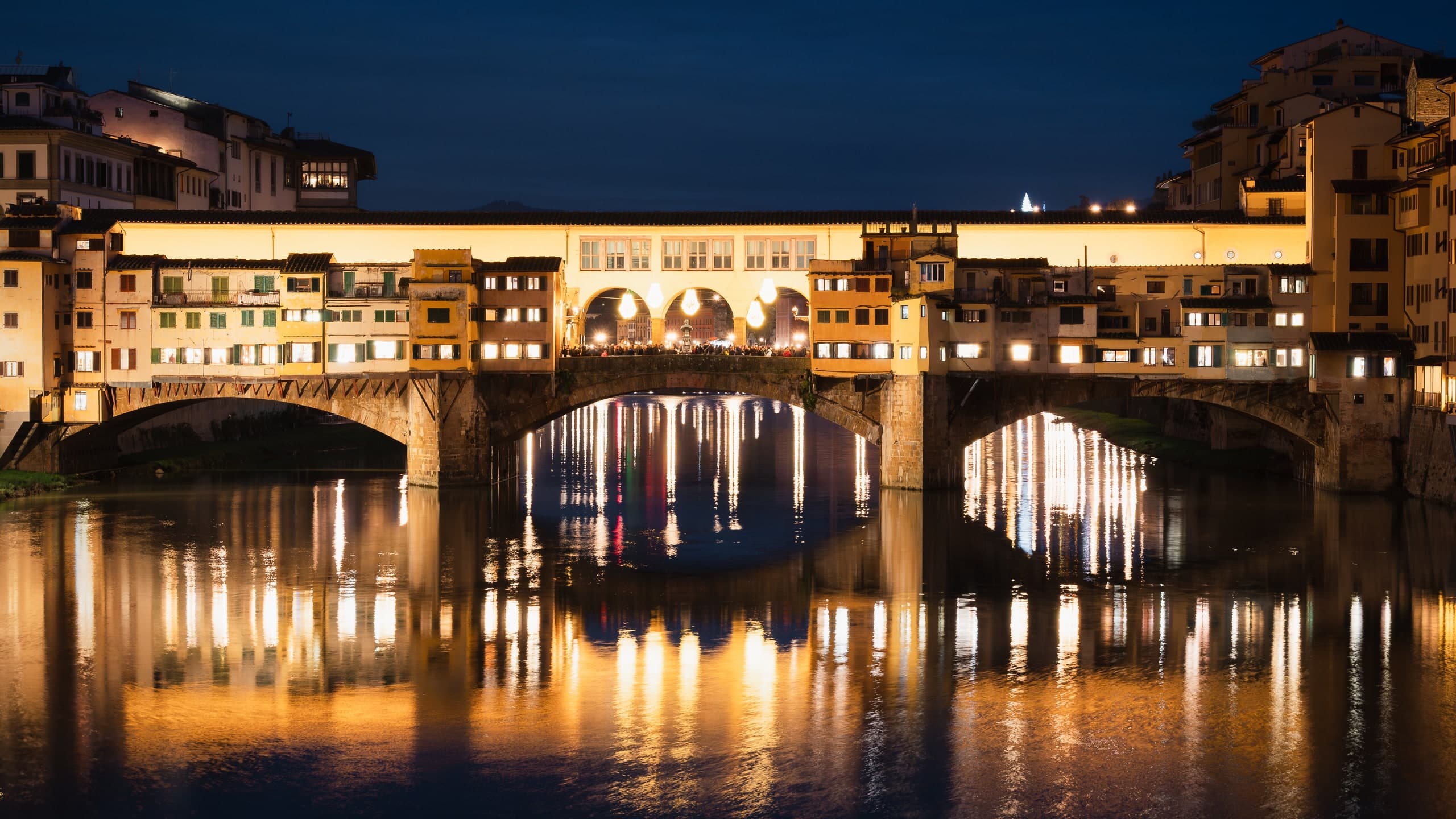 The Ponte Vecchio in Florence, lit and reflected in the Arno at night.
