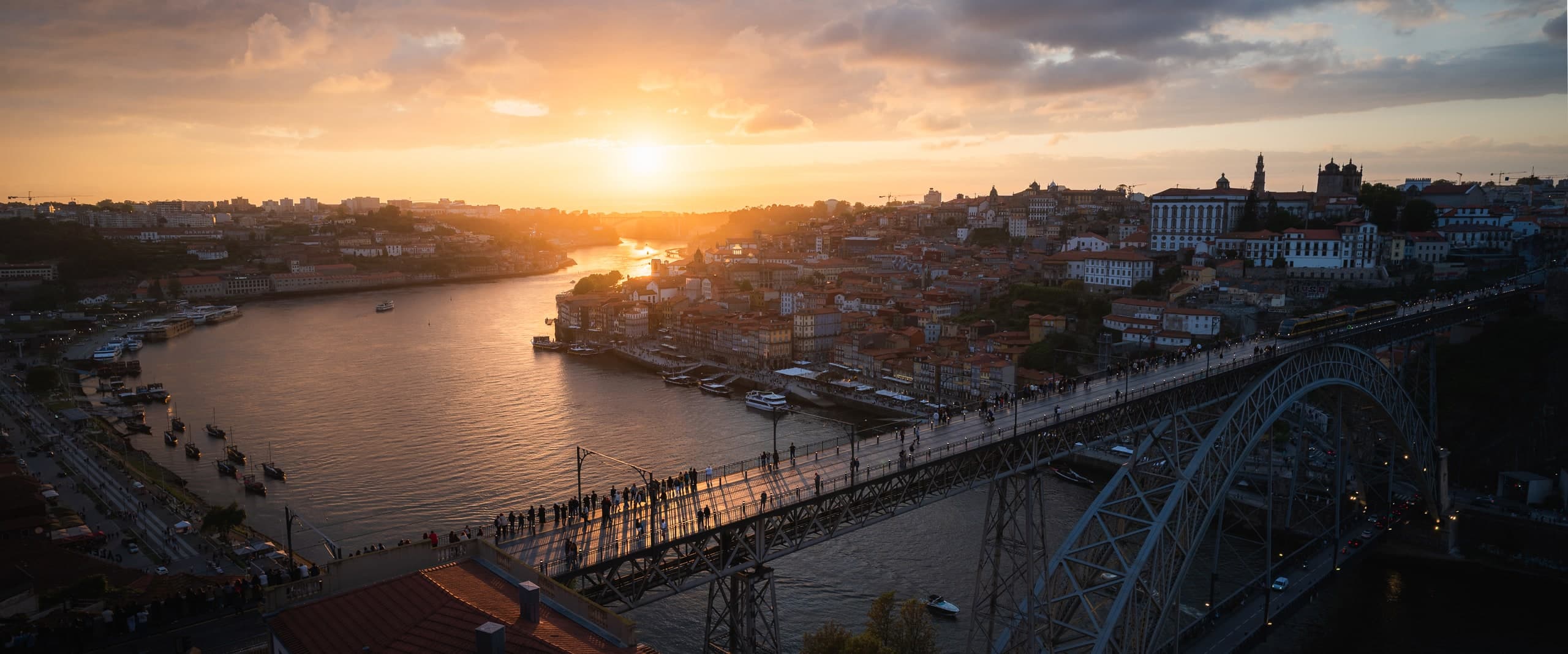 A wide view over Porto, Portugal at sunset, a bridge crossing the river below.
