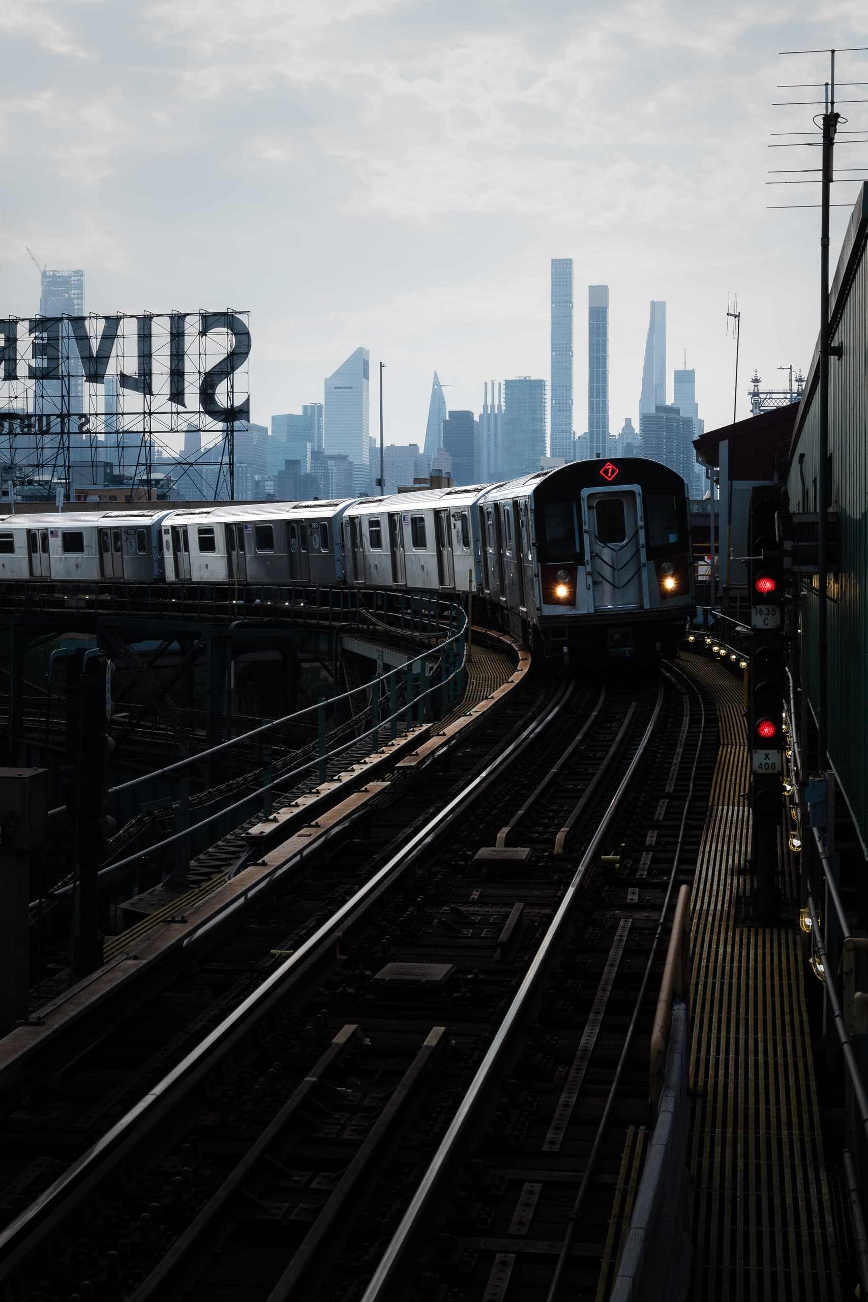 The 7 train arriving in Queens, the Manhattan skyline and the Silvercup Studios sign behind it.