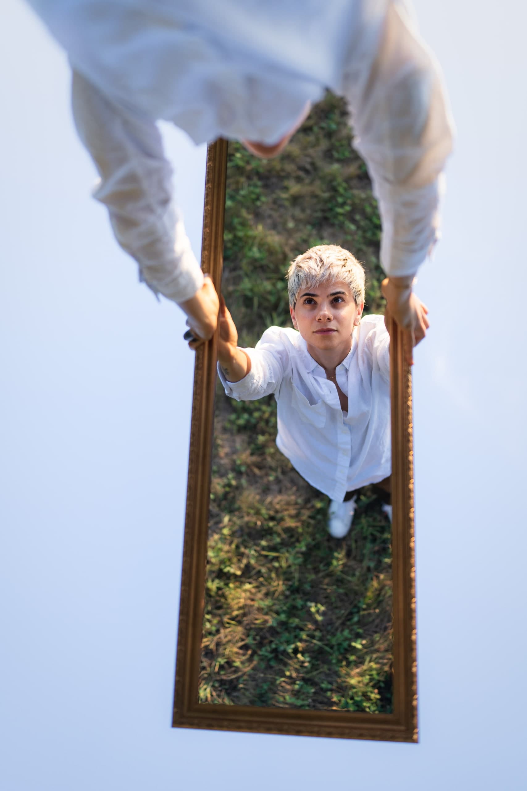 An overhead view of a woman looking up through a framed mirror standing in a field.
