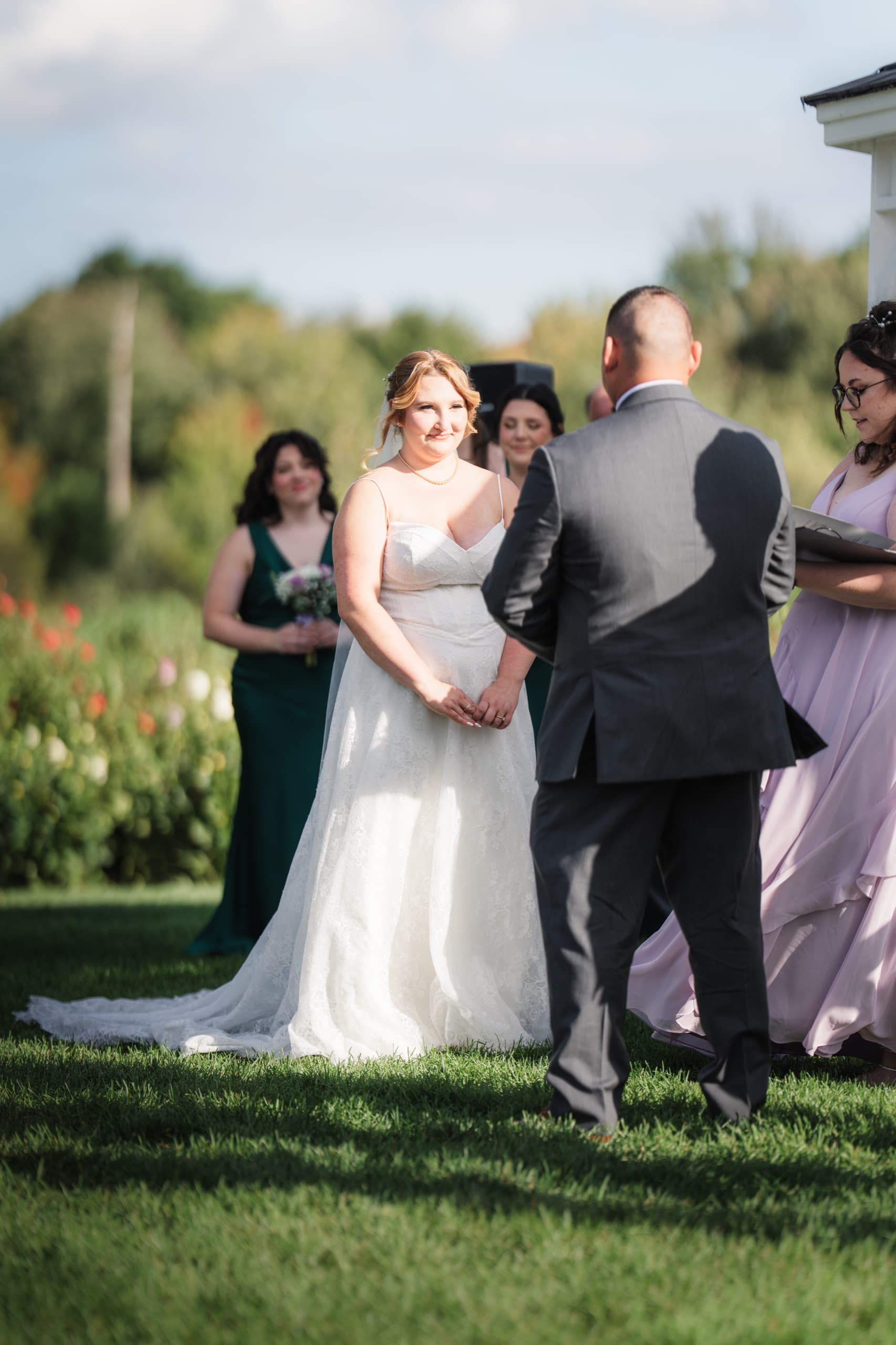 A bride and groom facing each other during their vows, bridesmaids and an officiant looking on.