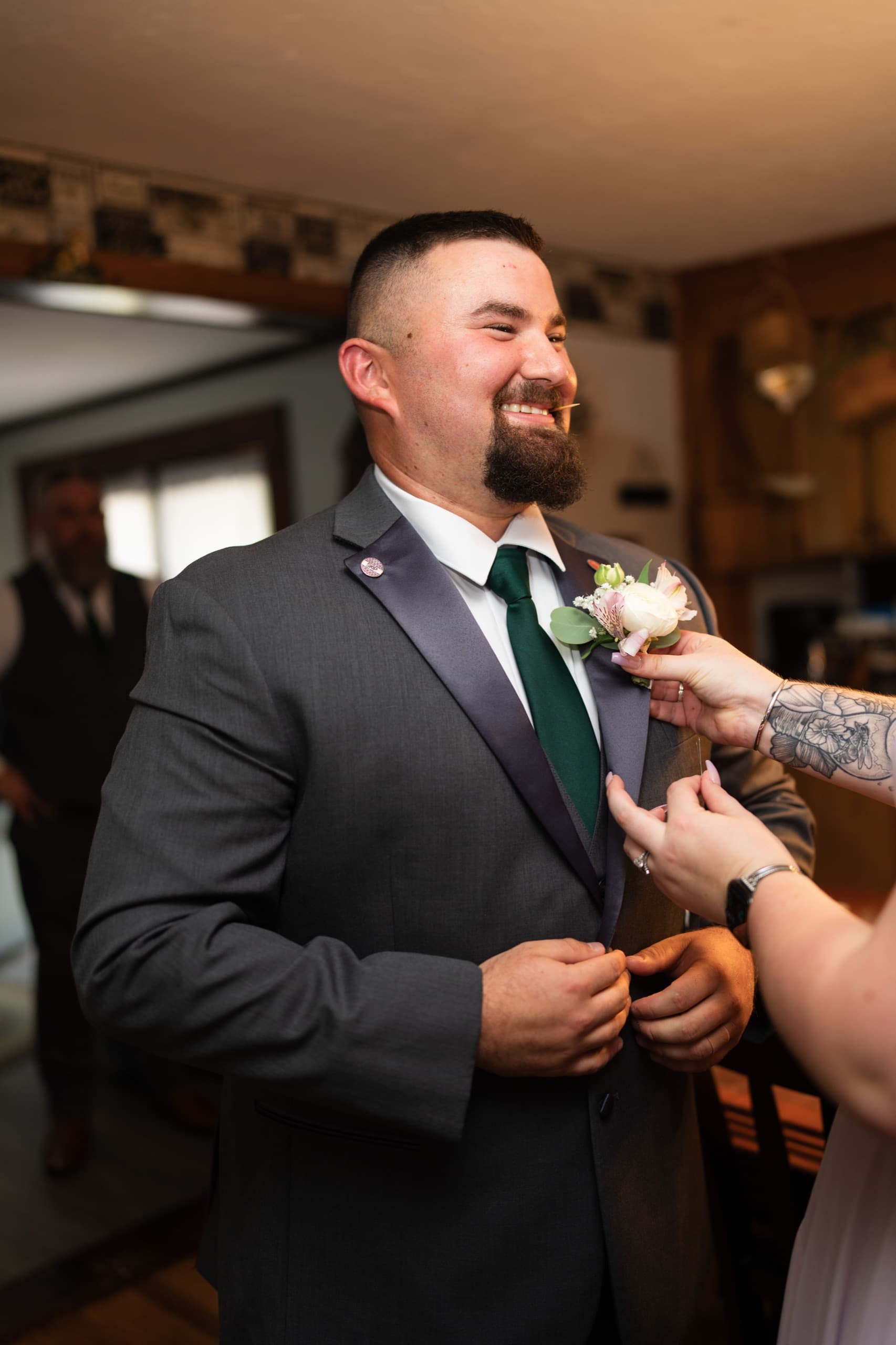 A groom laughing as his boutonniere is pinned on before the ceremony.