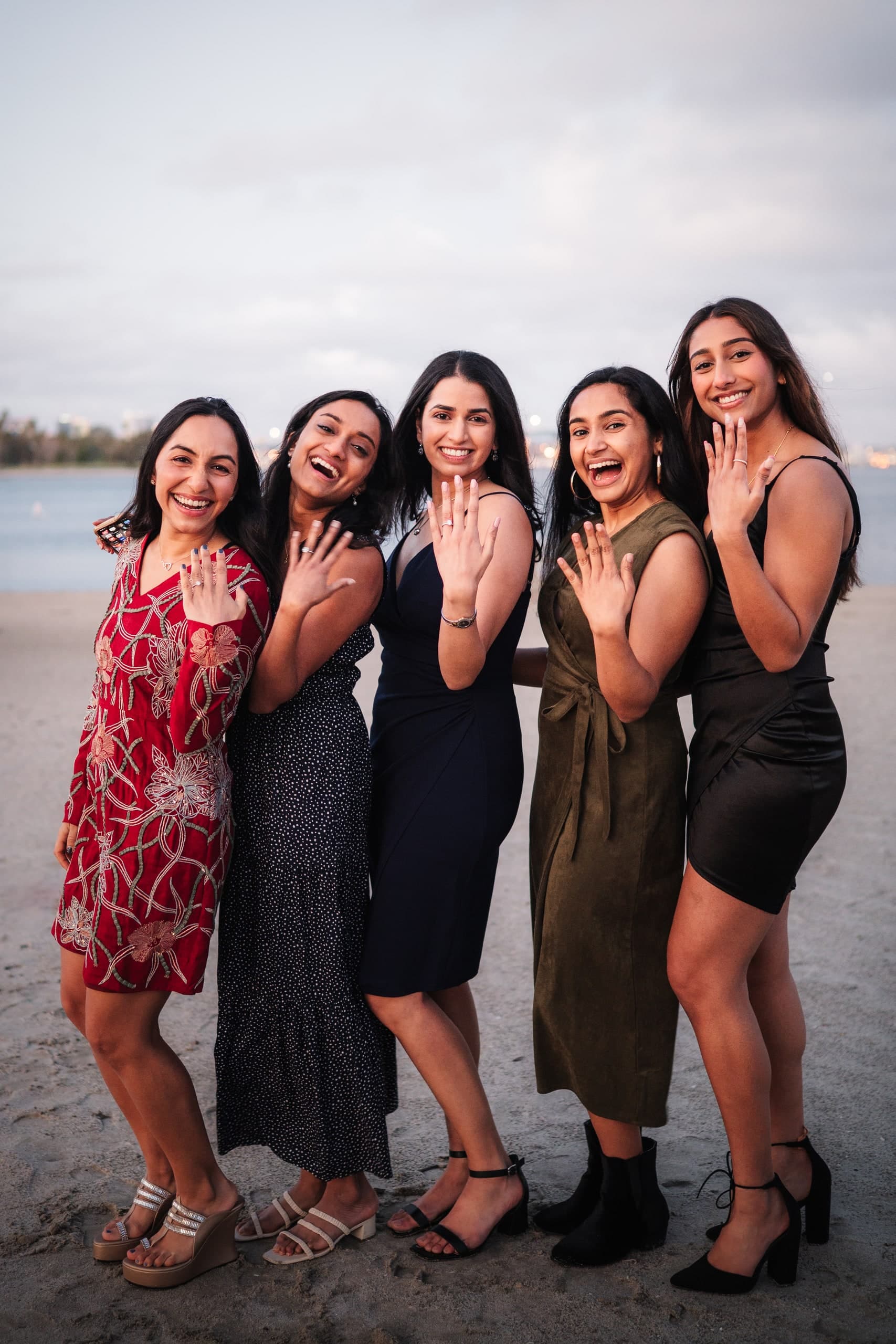 Four friends cheering together on an overcast beach, one holding up a ring.
