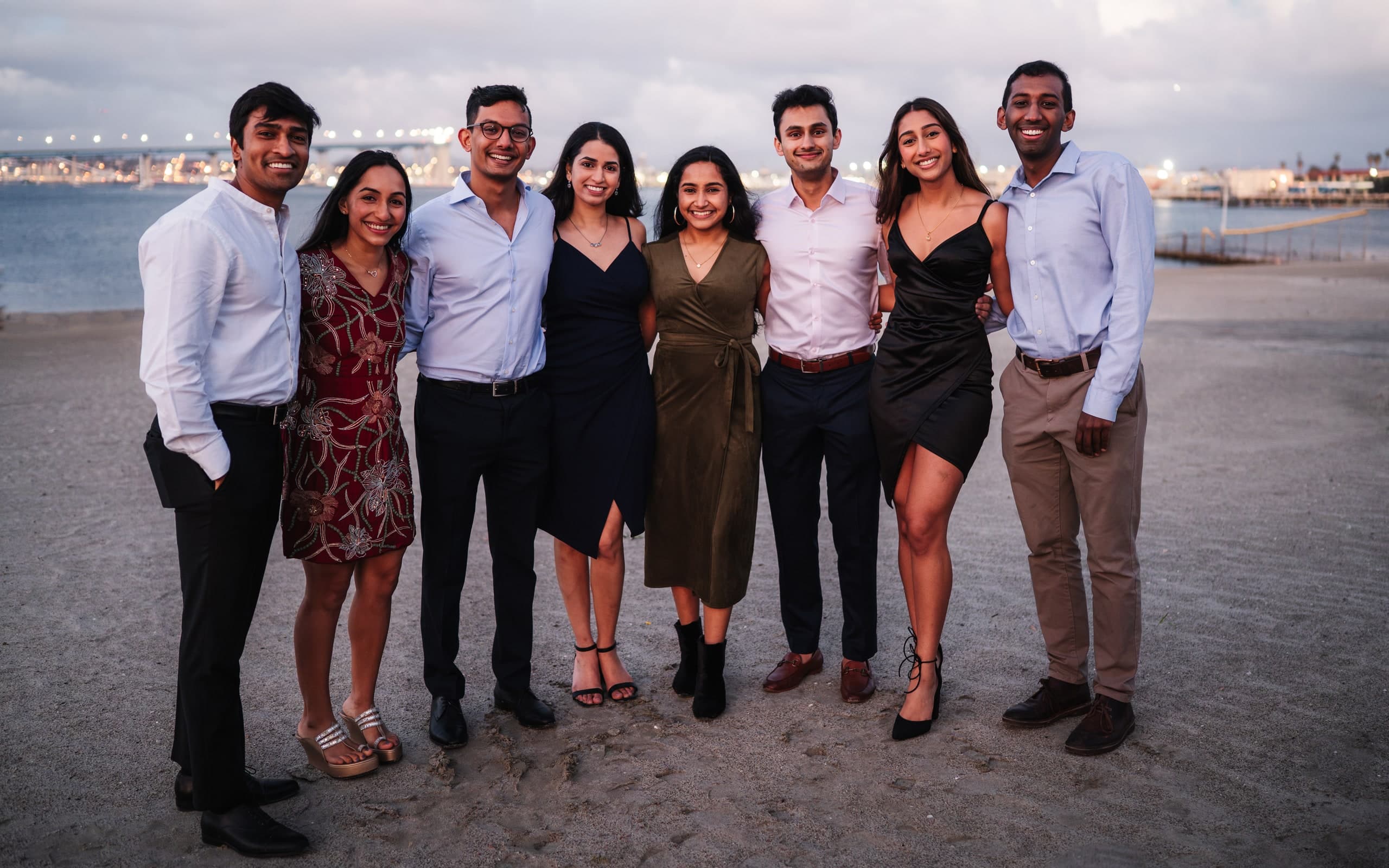 A group of eight friends posing together on the beach at dusk.