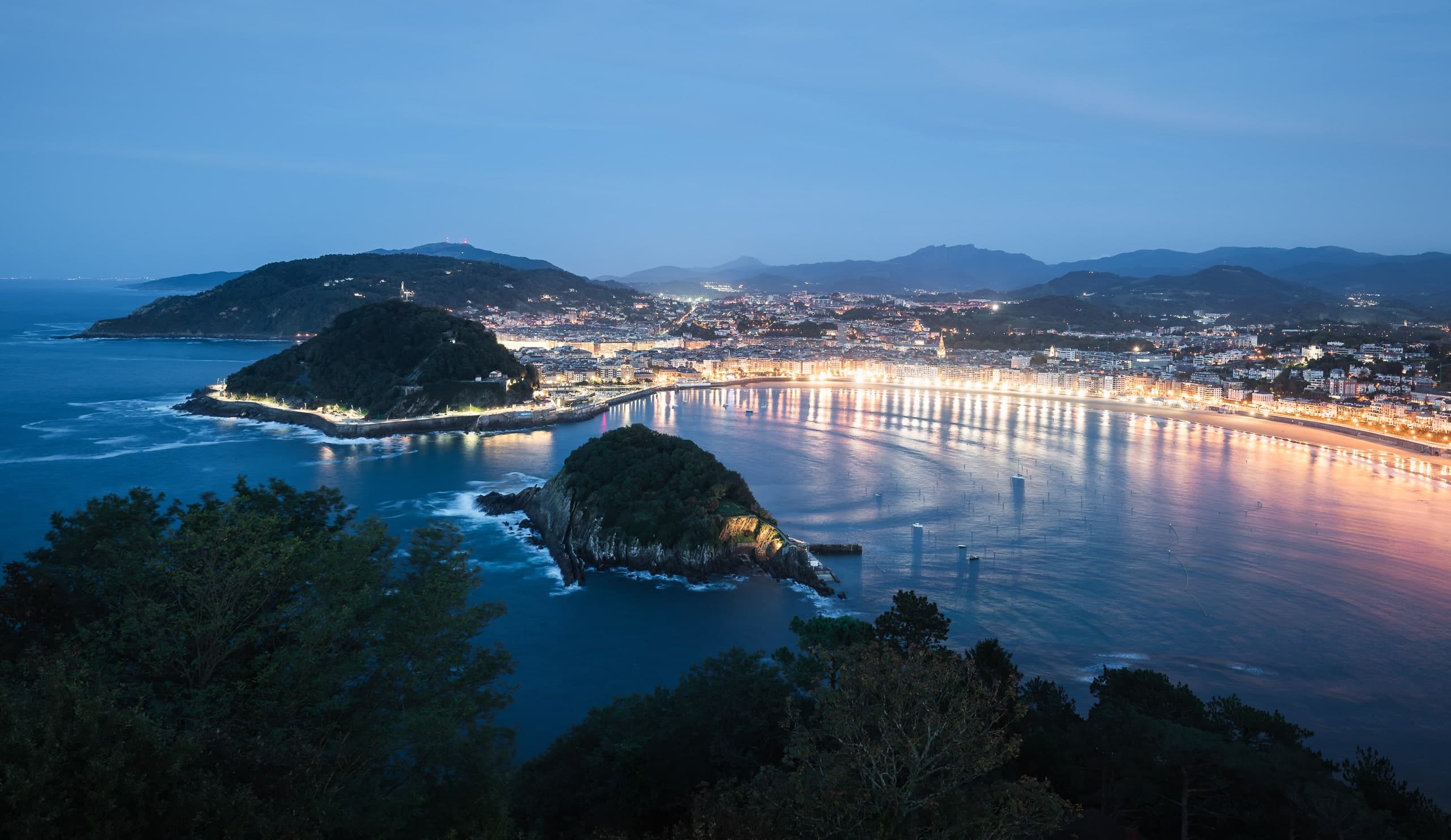 An aerial view of San Sebastián’s bay at dusk, the city lights curving around the shoreline.