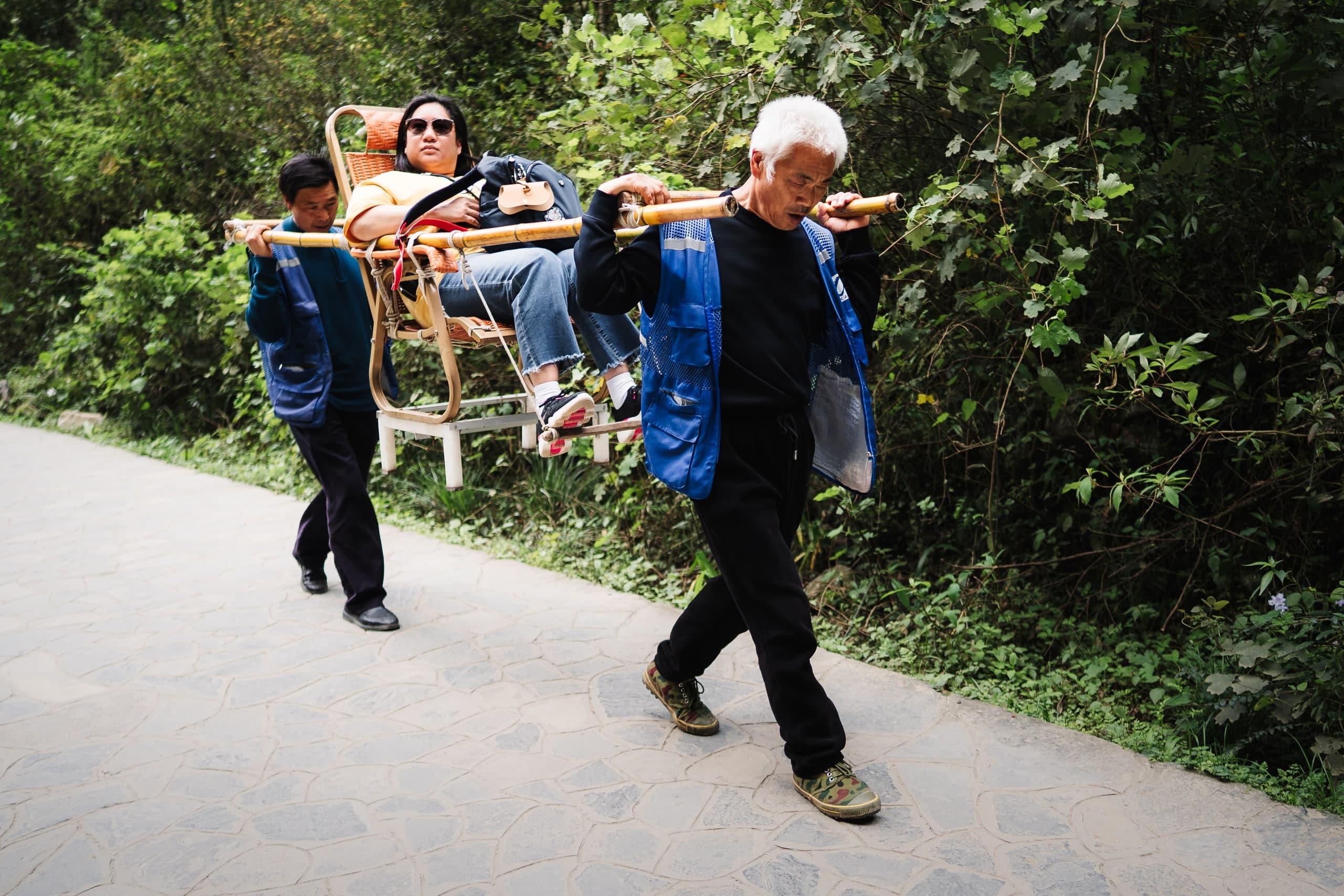 Porters carrying a woman in a sedan chair up a mountain path in China.