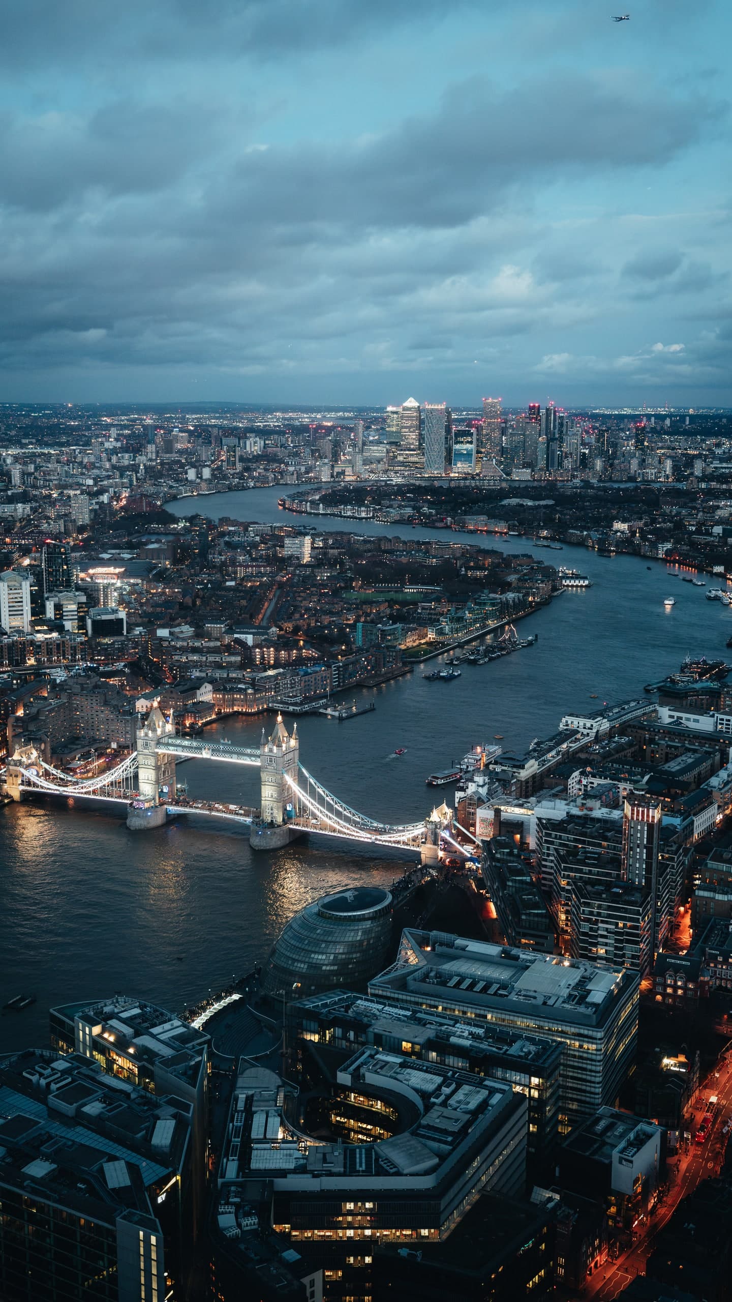 An aerial view of London at dusk, Tower Bridge lit and the Thames curving through the city.
