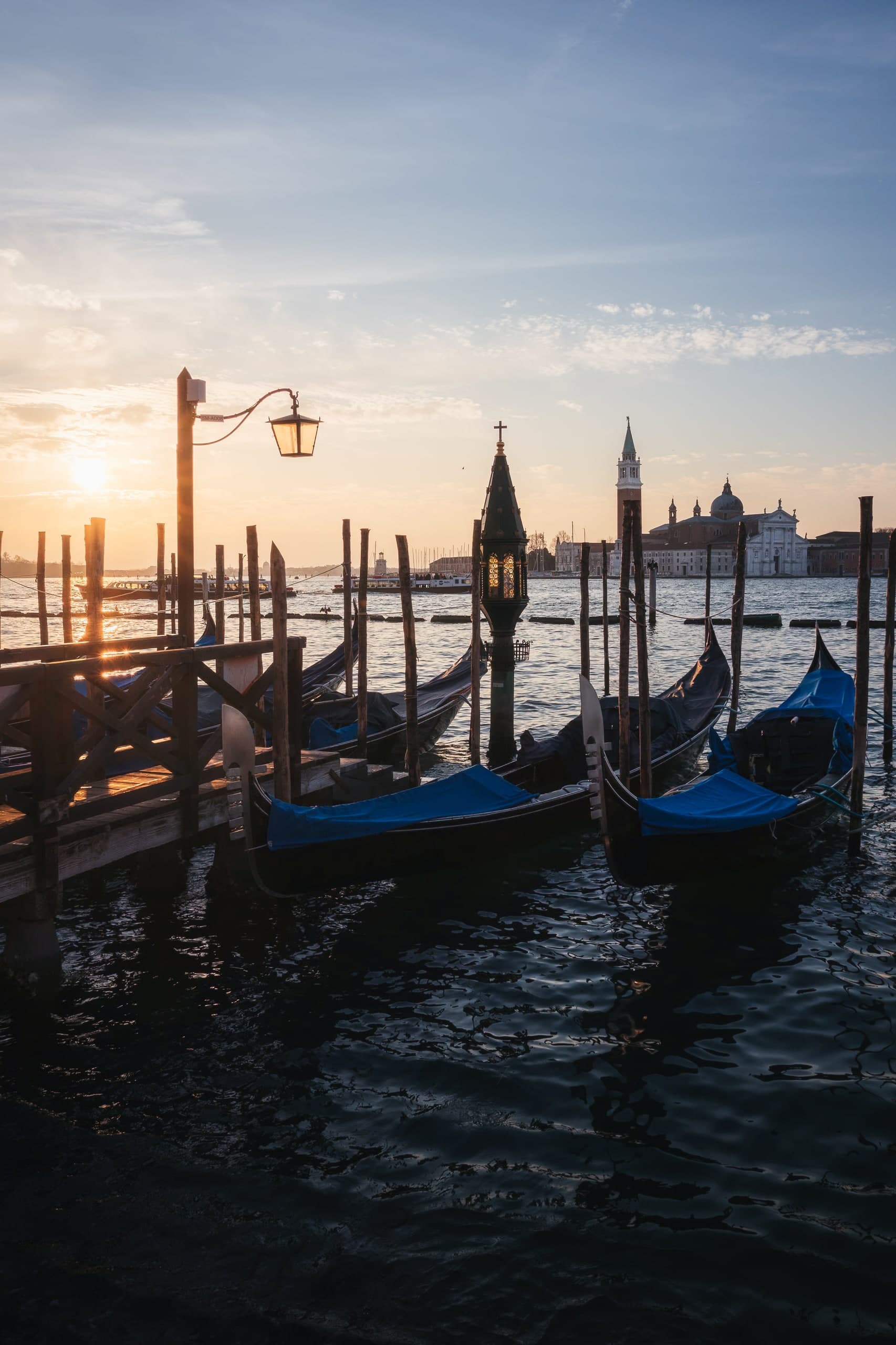 Gondolas moored in Venice at sunset, a church silhouetted across the water.