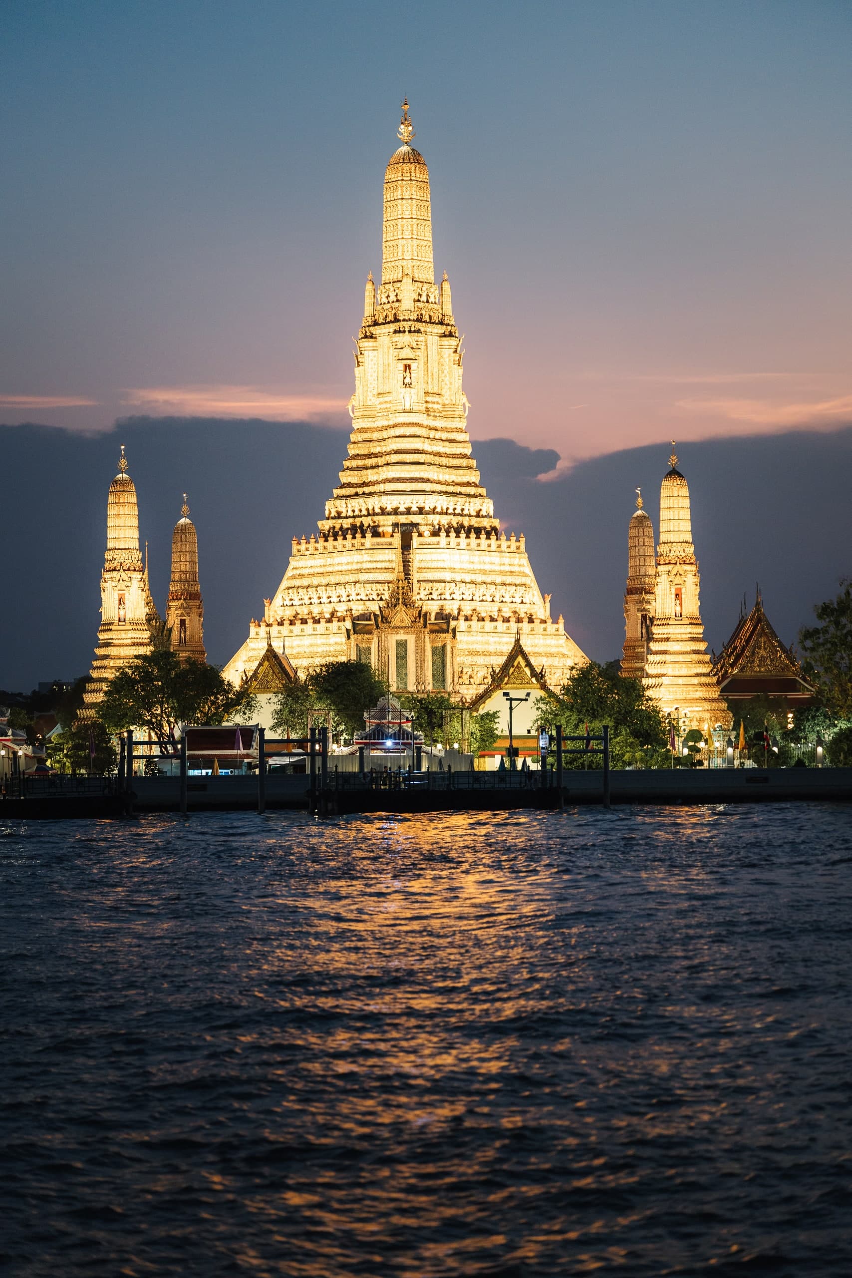 Wat Arun temple in Bangkok lit at dusk, seen across the river.