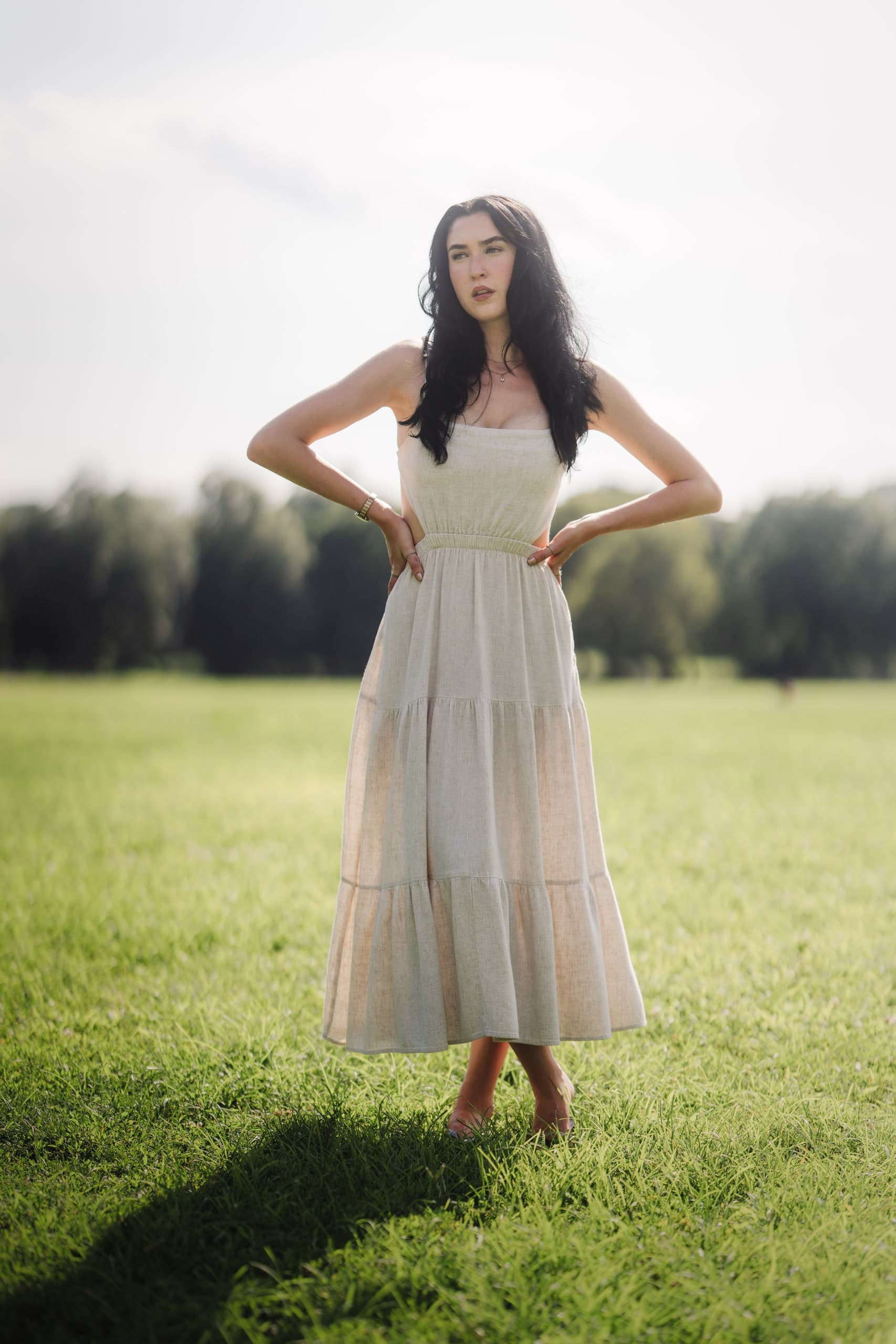 A woman in a tiered cream dress standing in an open field, hands on her hips.